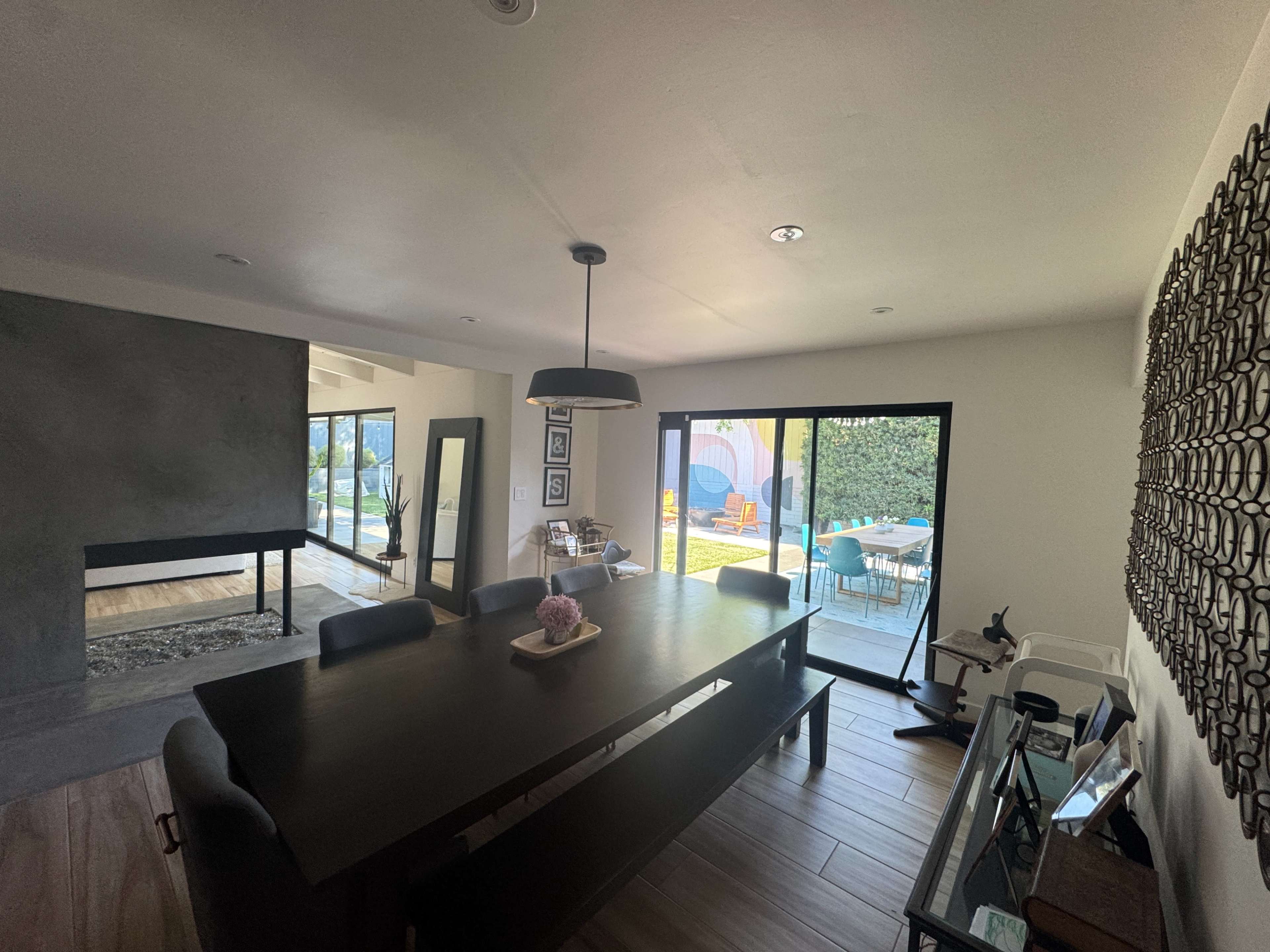 The image shows a modern dining area with a large table, black chairs, and sliding glass doors leading to an outdoor patio.