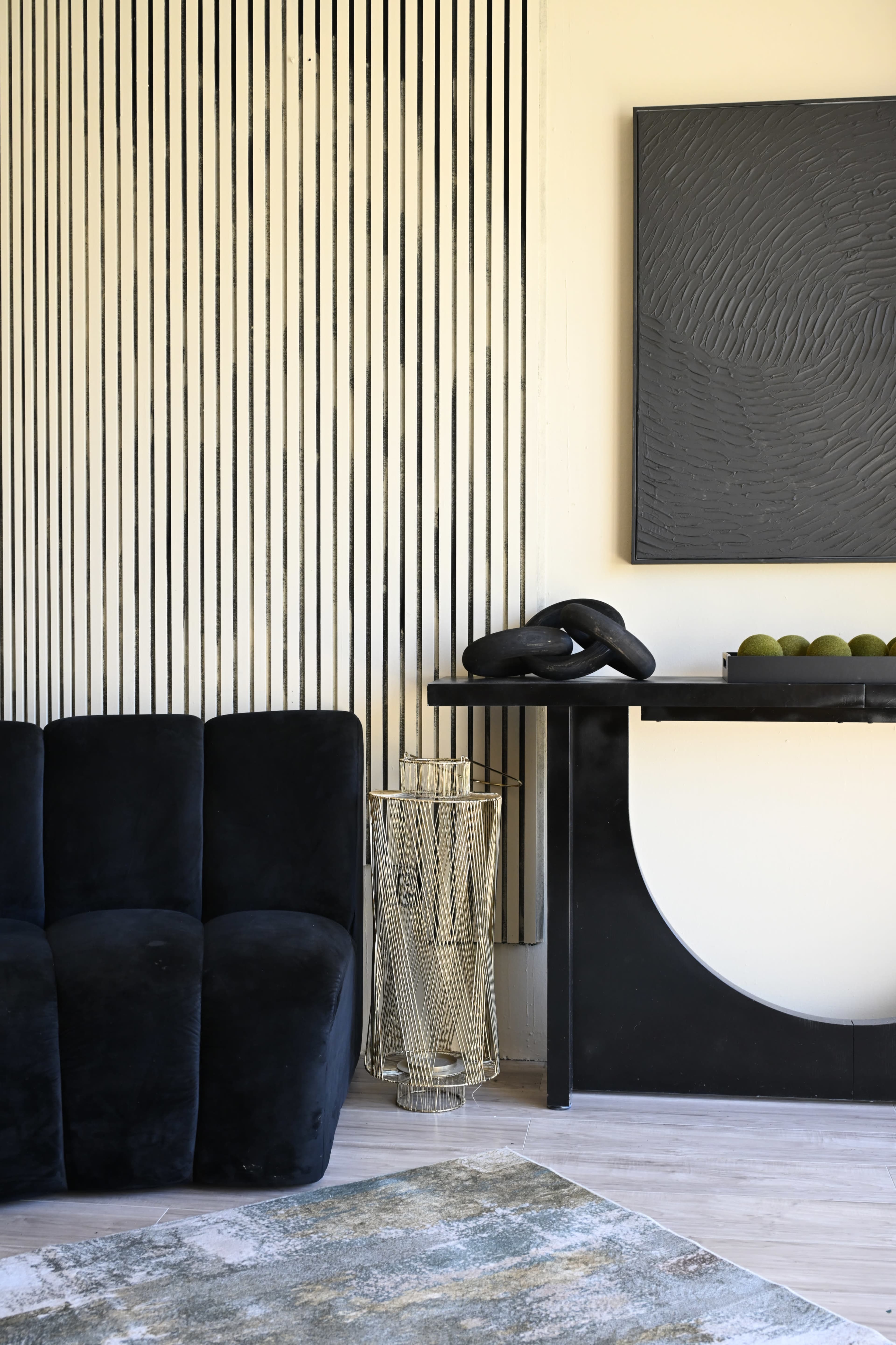 The image shows a modern living space featuring a dark, upholstered sofa, a black console table with decorative elements, and a striped wall in the background.