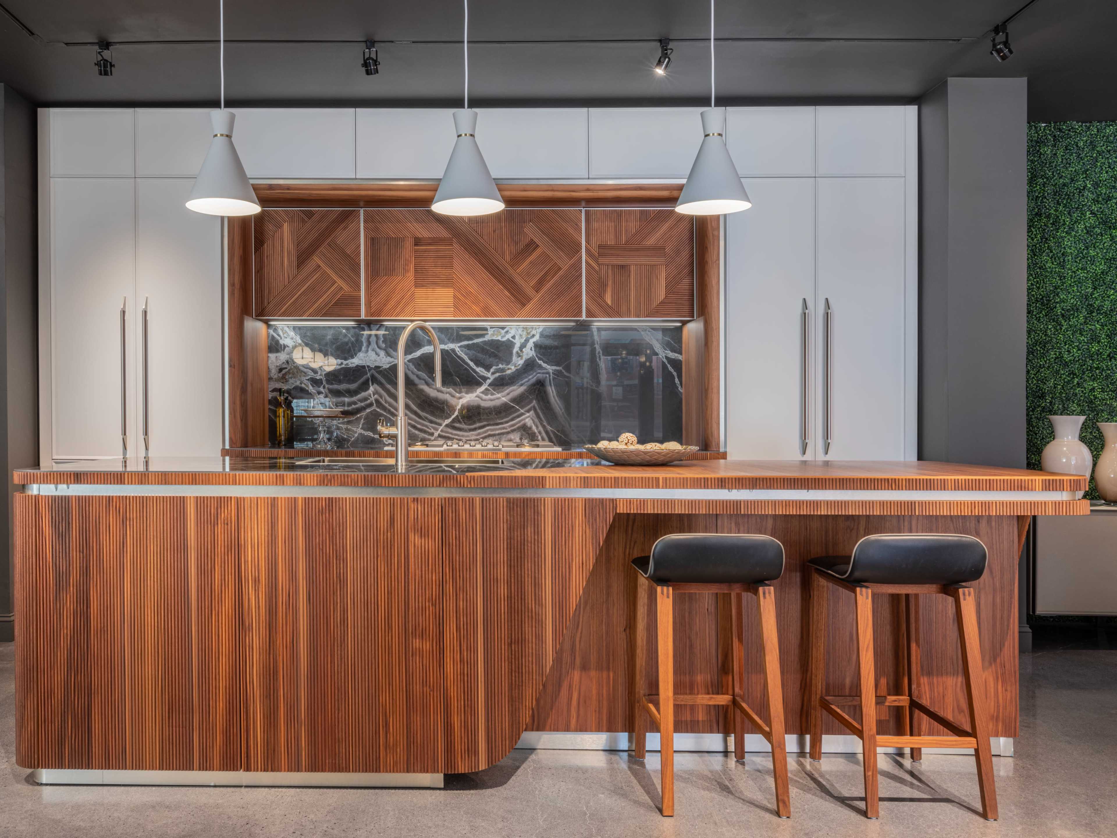 A modern kitchen features a wooden island with two black stools, white cabinets, and pendant lighting above.