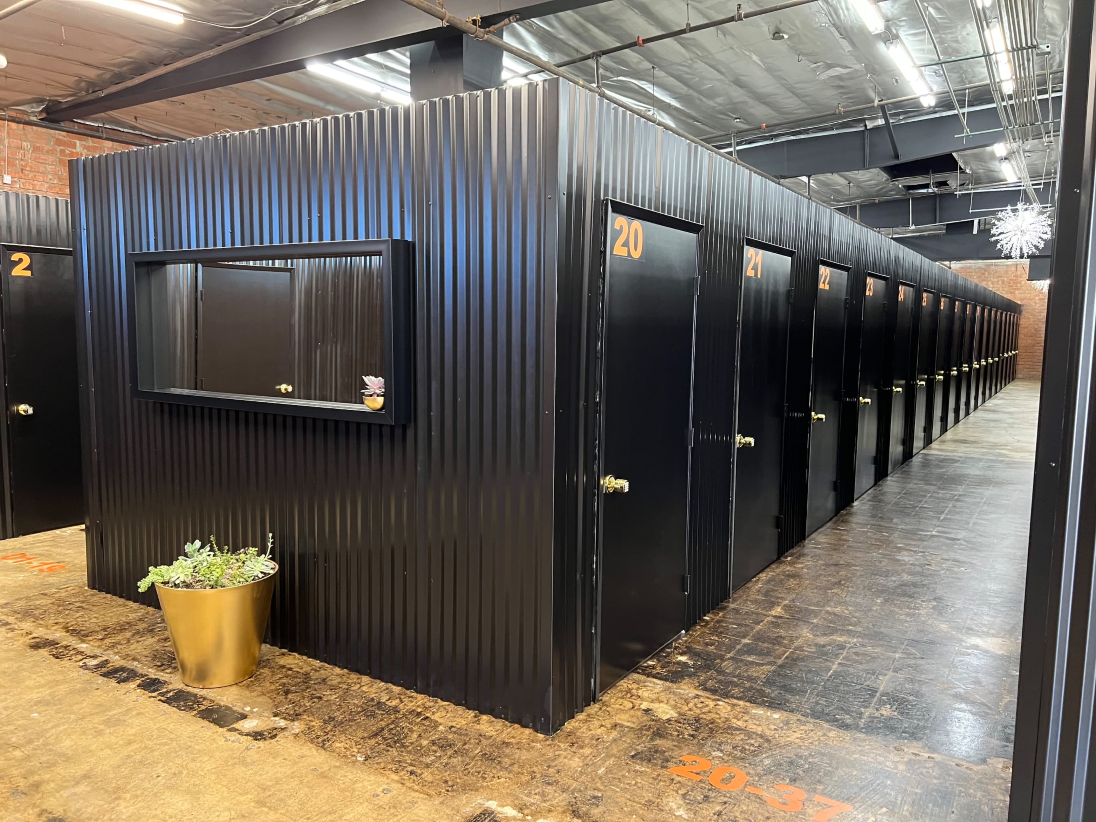 The image shows a row of metallic storage units with black doors, arranged in a warehouse-like space.