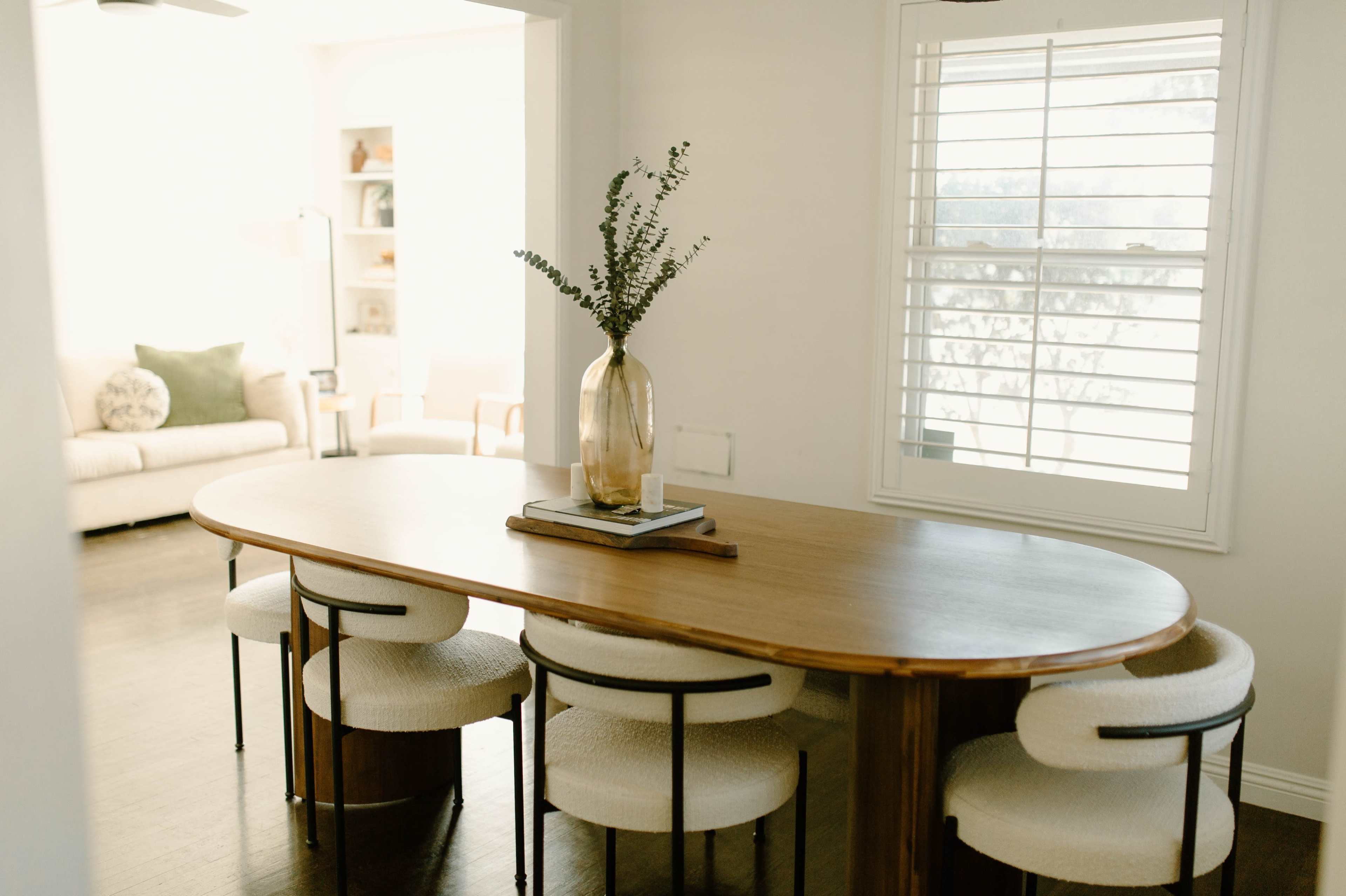 A wooden table surrounded by upholstered chairs is positioned near a window in a well-lit dining area.