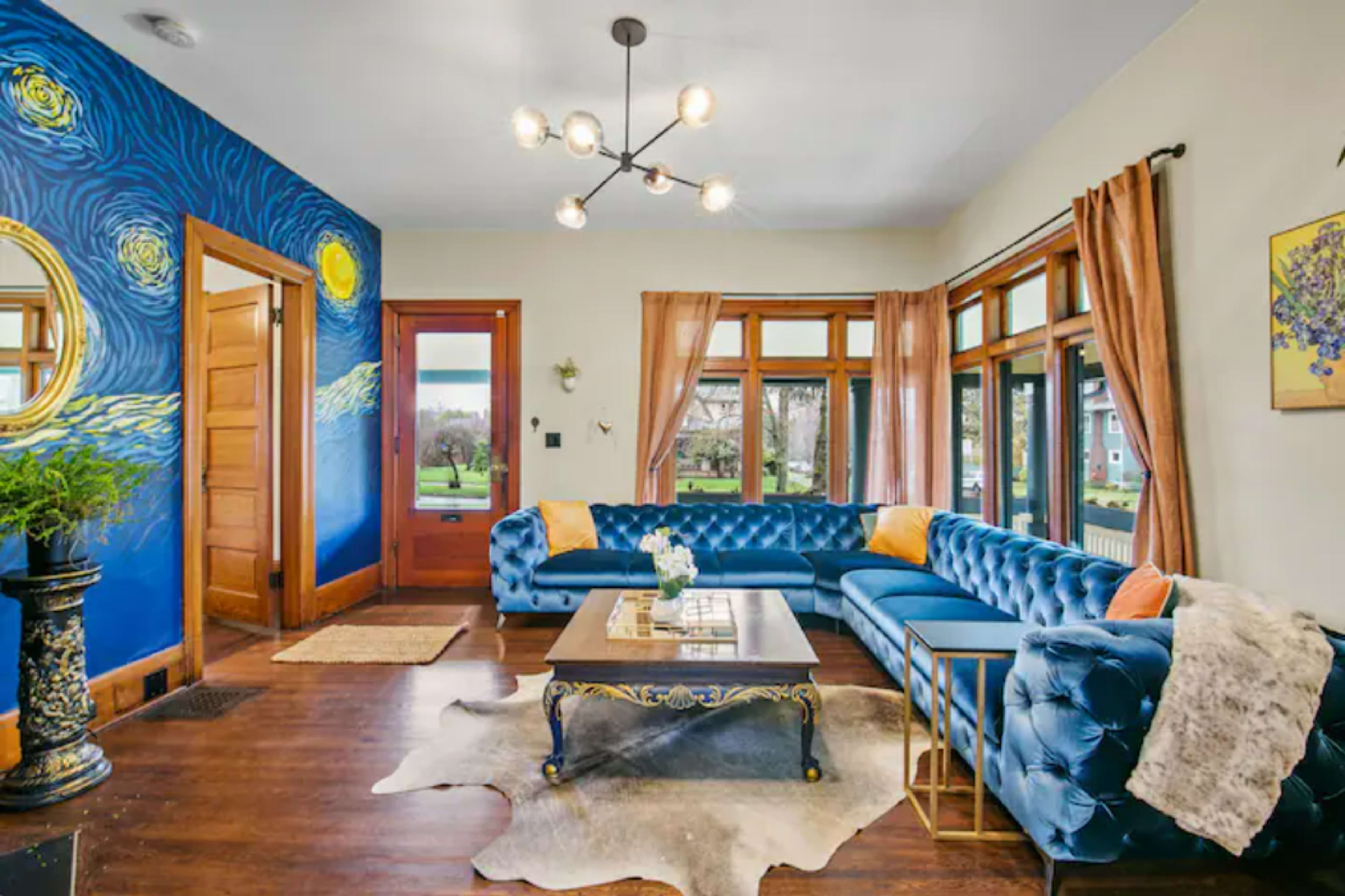 A living room with a blue wall featuring a starry design, a large blue sectional sofa, a coffee table, and large windows letting in natural light.