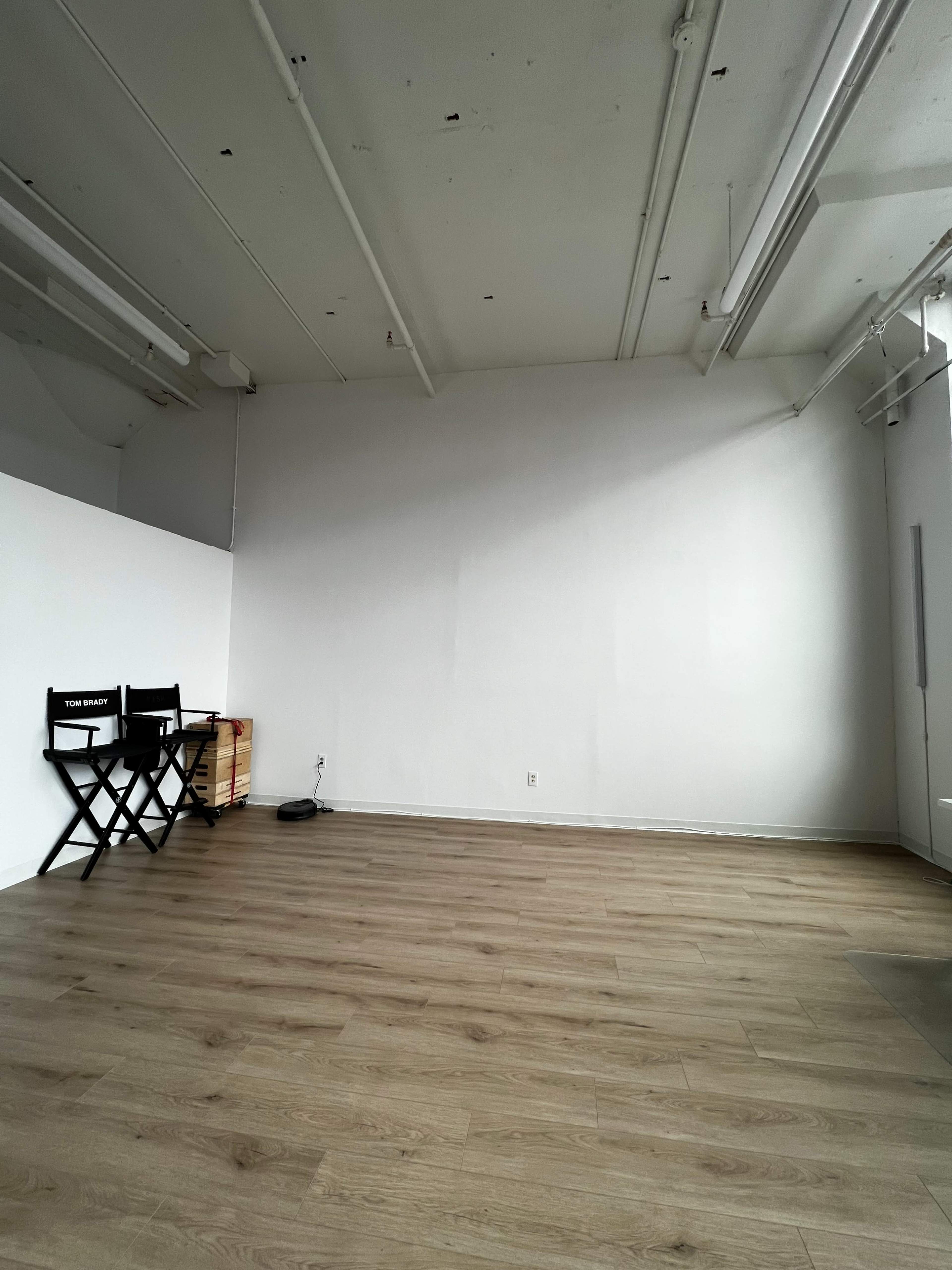 The room features a vacant wall, wooden flooring, a folding chair, and a small table.