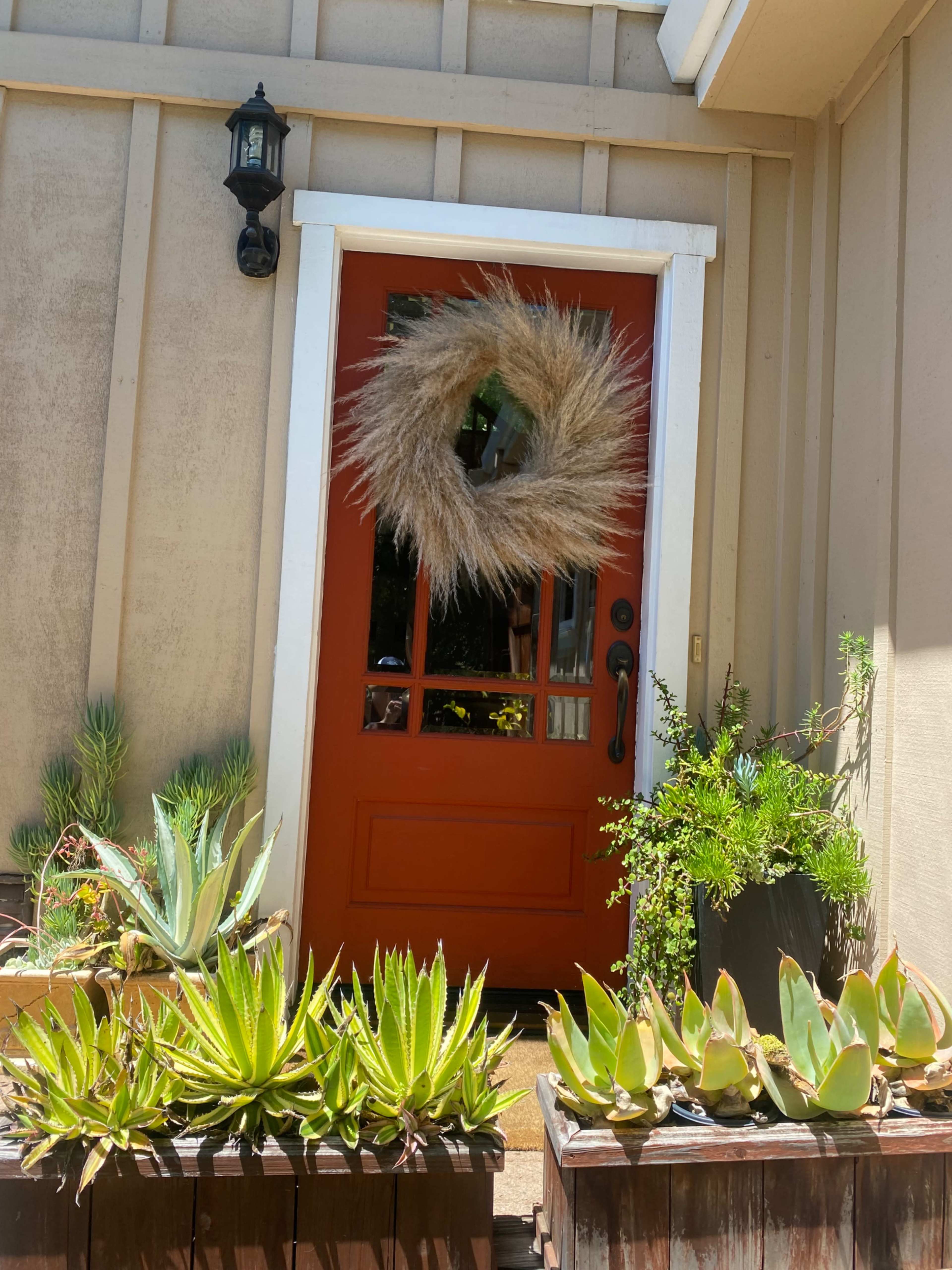 A front door painted in orange, adorned with a decorative wreath, surrounded by planters filled with various succulents.