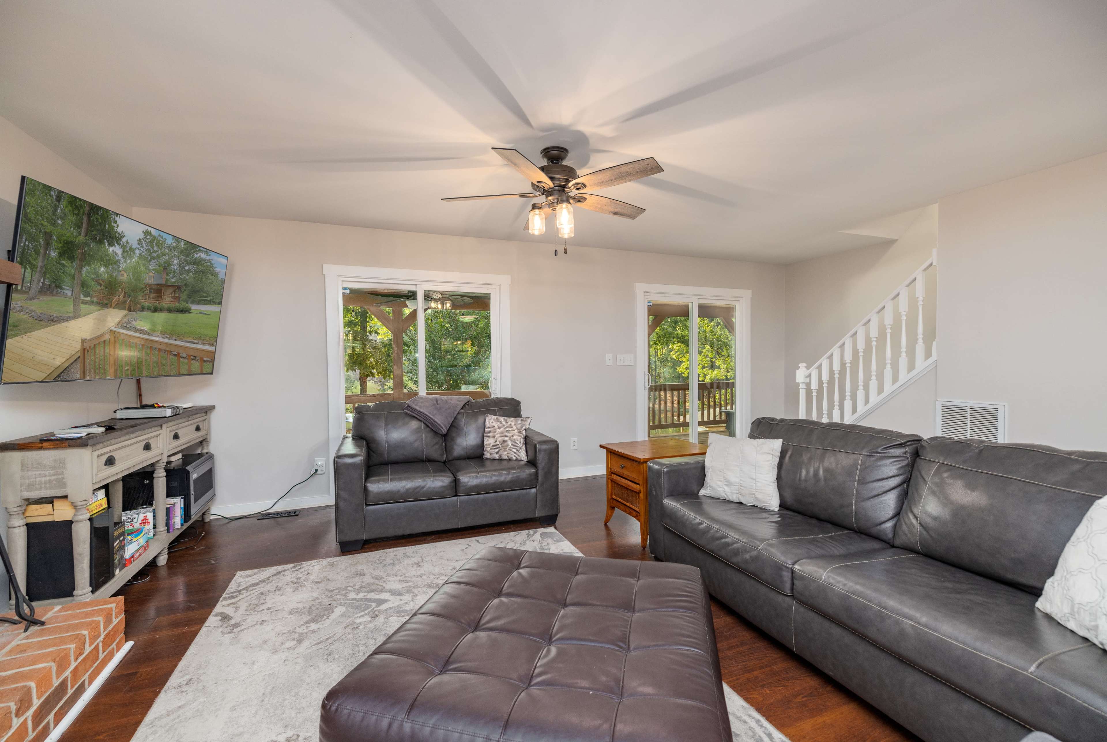 A living room features a television on the wall, two leather sofas, a coffee table, and a staircase leading to an upper level.