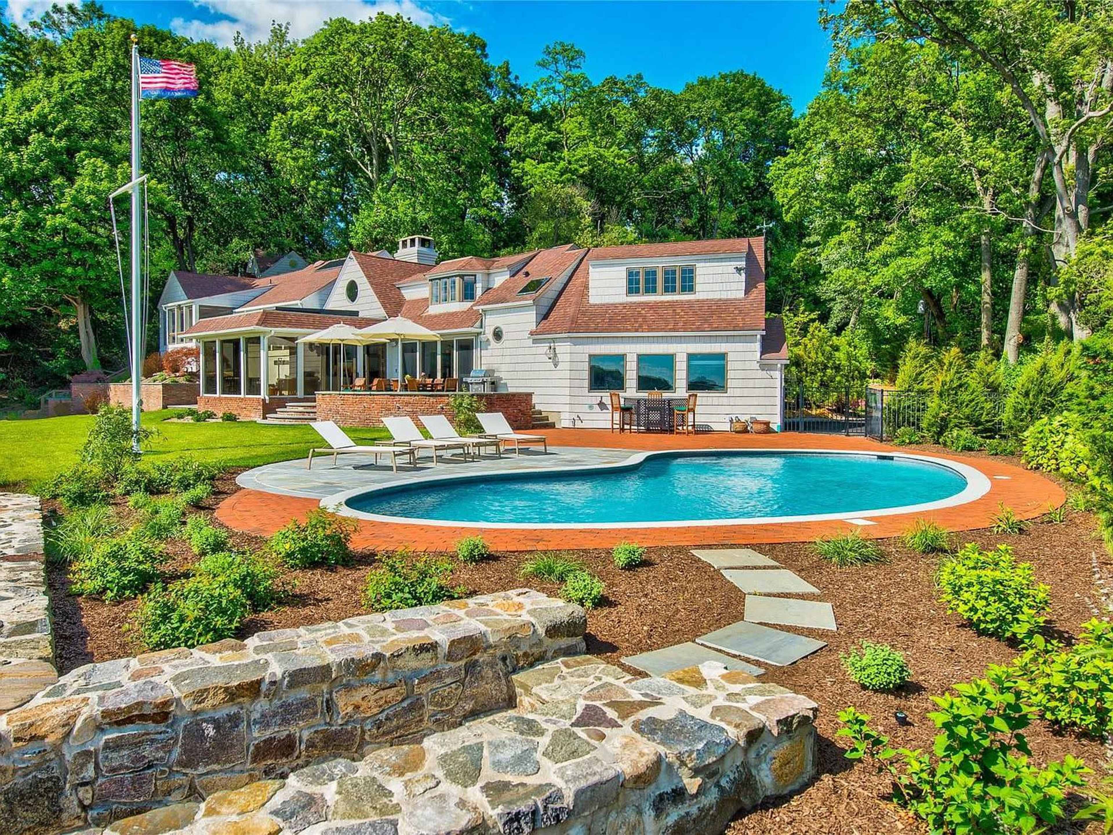 The image shows a landscaped backyard with a swimming pool, patio, and a house surrounded by trees.