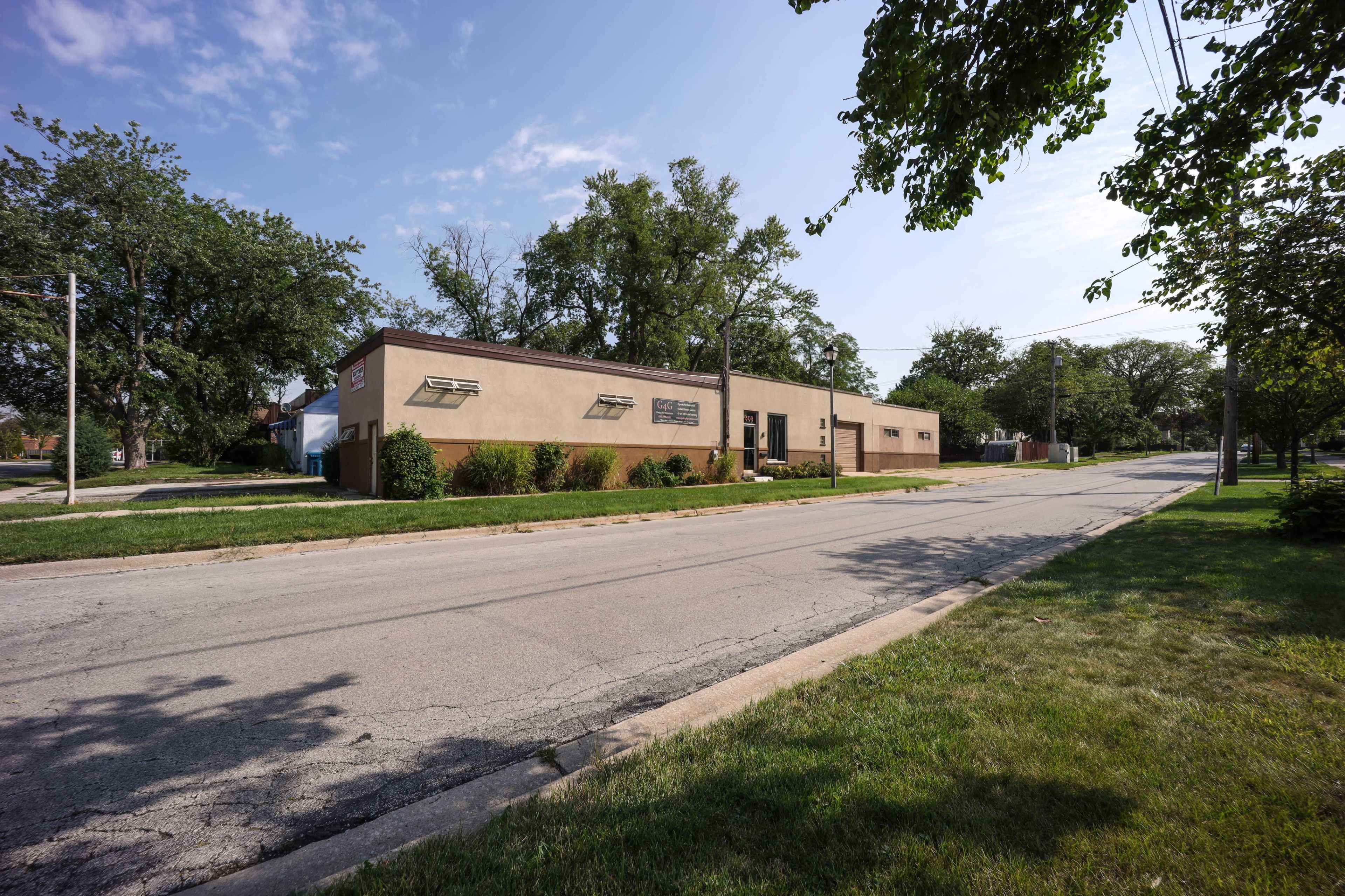 A single-story commercial building alongside a paved road, with trees and grass lining the street.