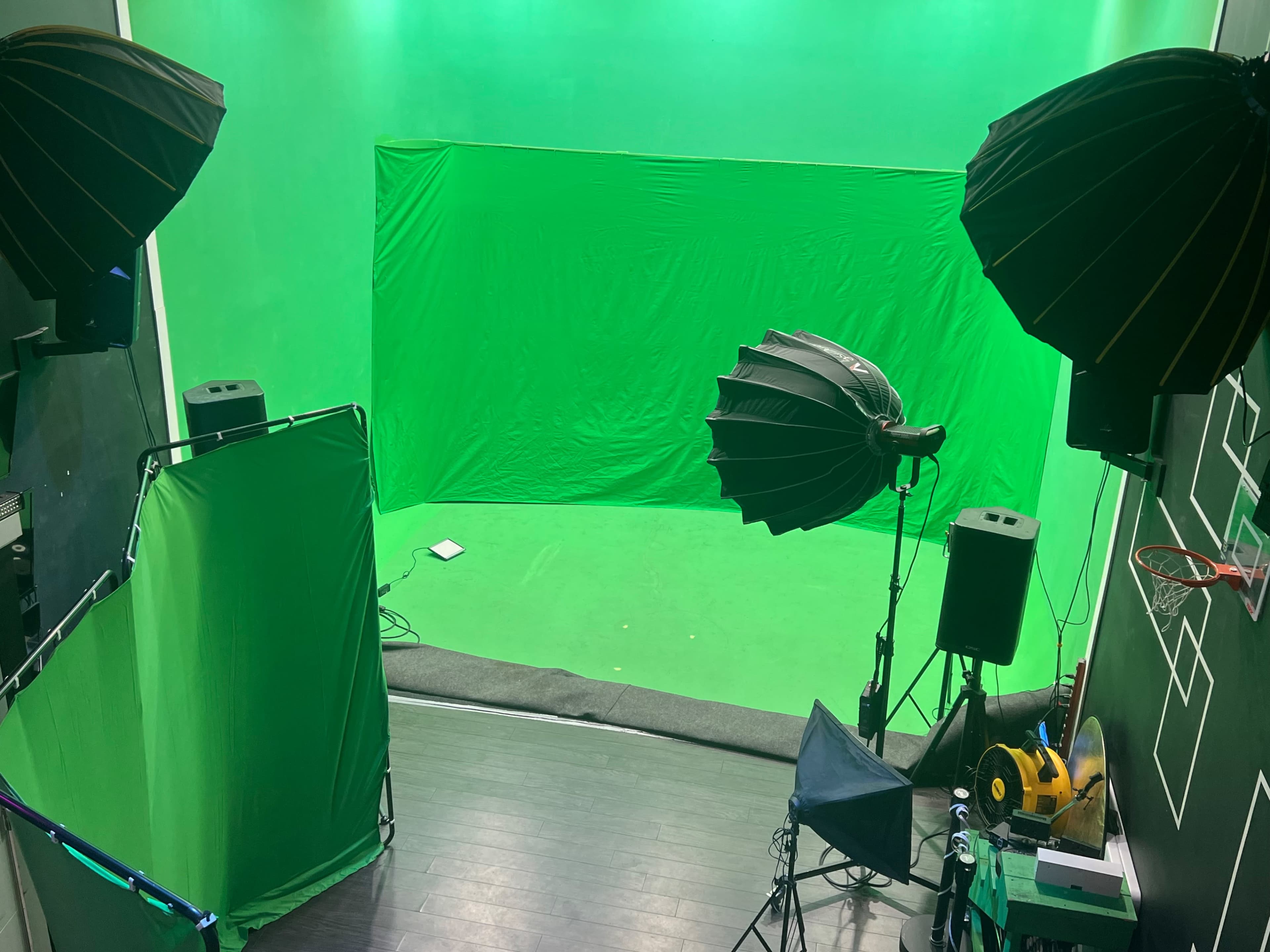 The image shows a green screen studio with various lighting equipment and a basketball hoop in the background.