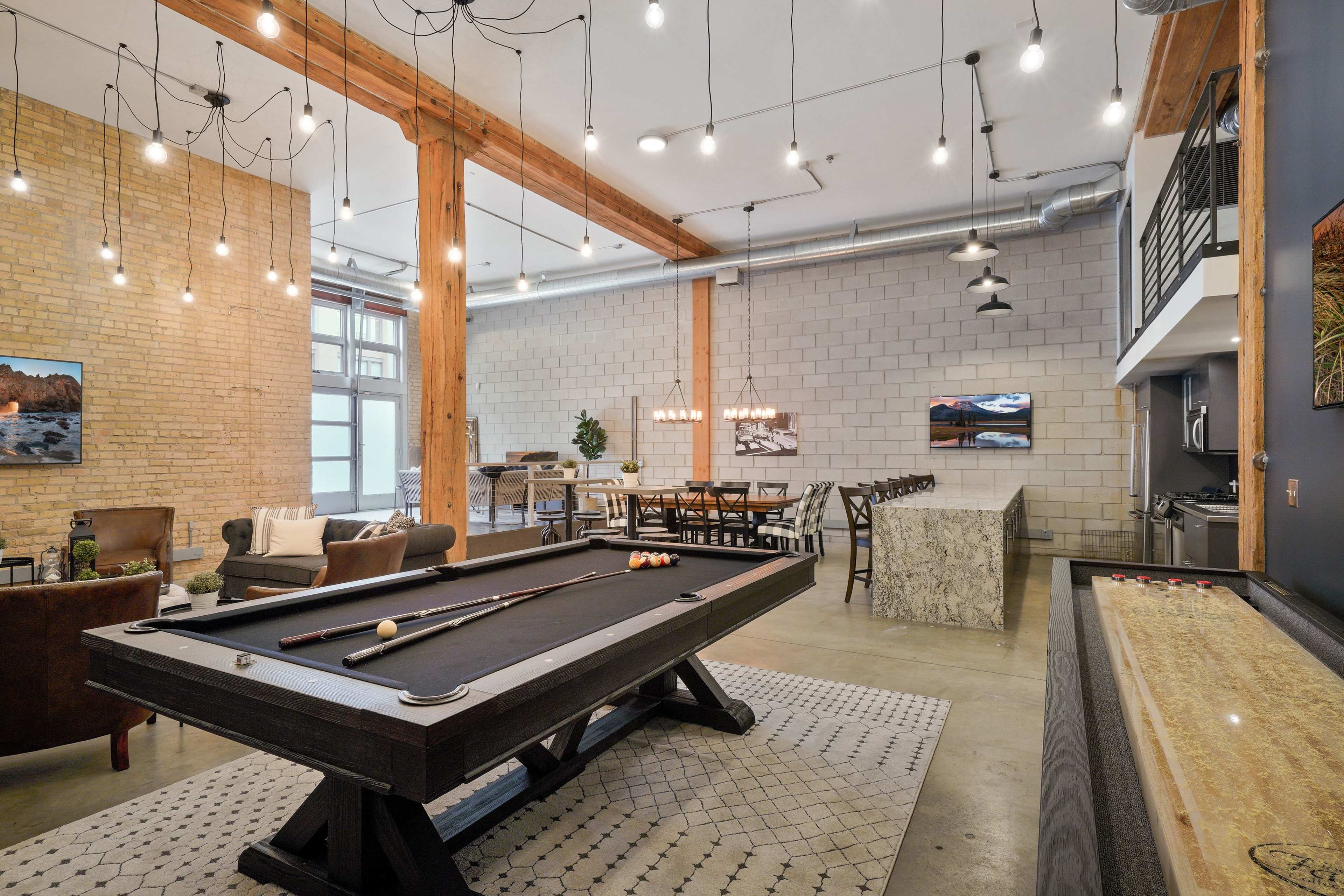 A spacious recreational area featuring a pool table, seating arrangements, a dining table, and a modern bar with a stone counter.