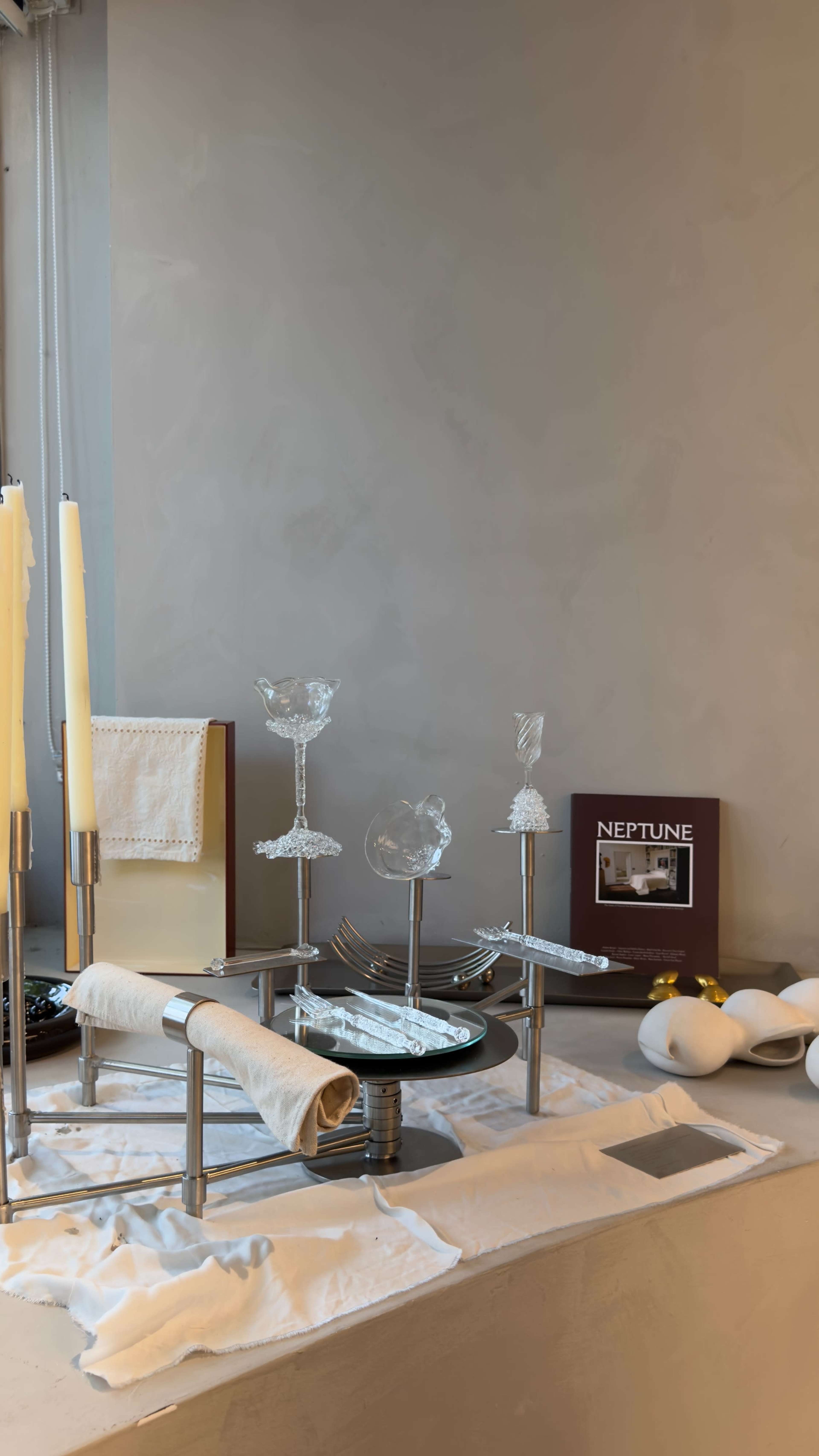 A table setting displays various glassware and utensils, accompanied by candles and a decorative book titled "Neptune."
