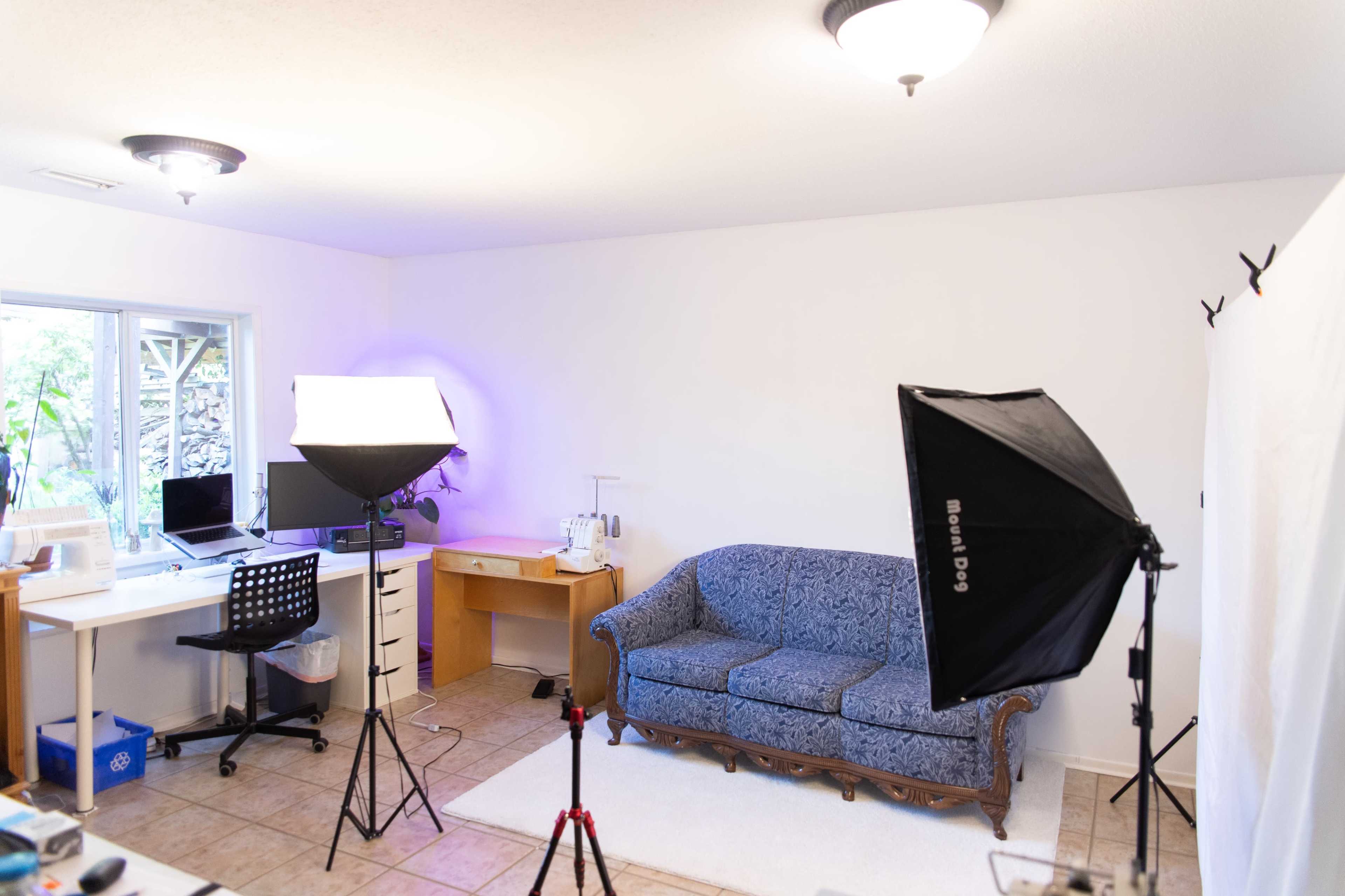 A well-lit, uncluttered room with a blue couch, a desk with a computer, and photography lighting equipment set up.