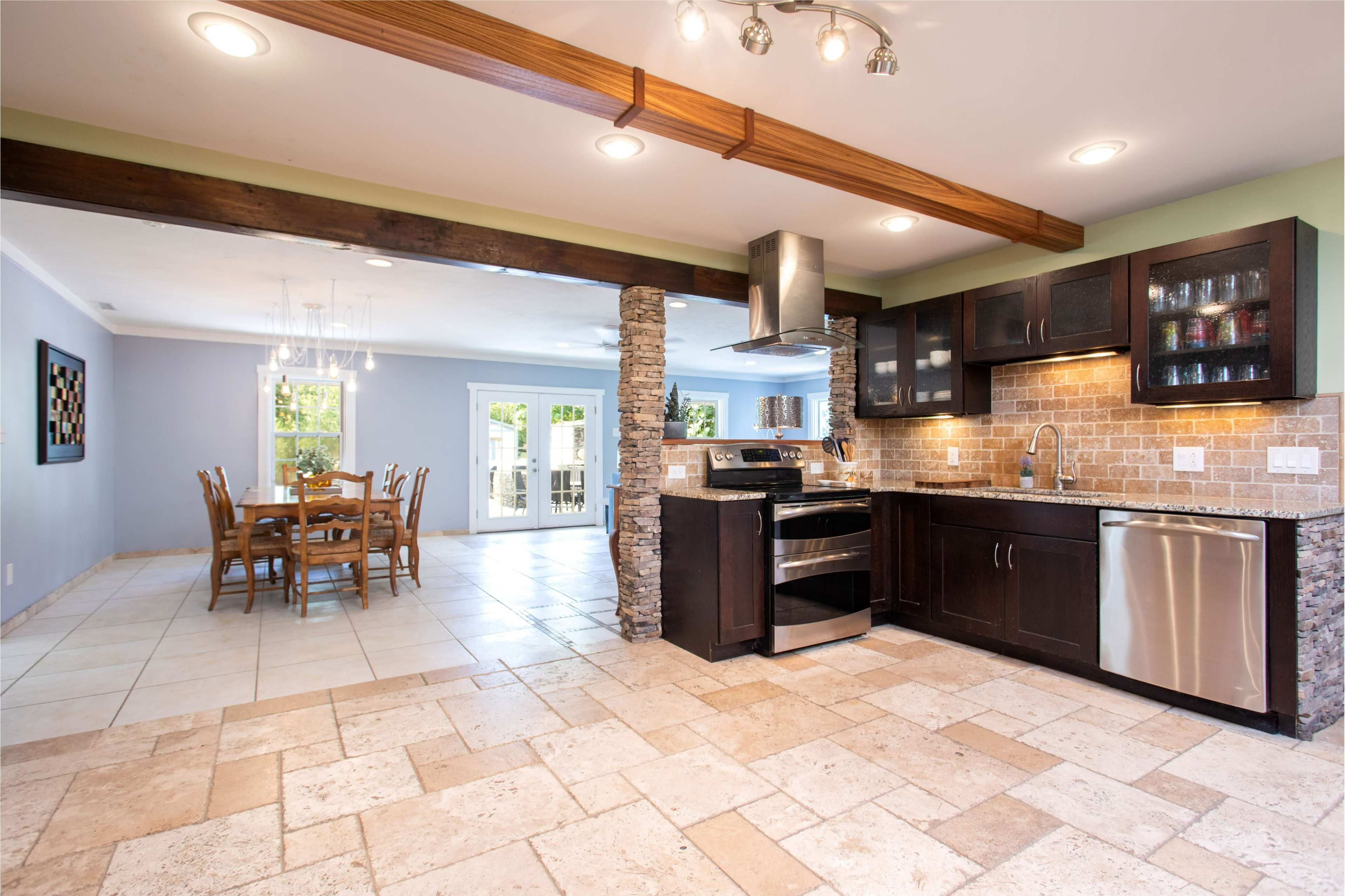 A modern kitchen with a stone accent wall, stainless steel appliances, and a tiled floor that connects to a dining area with wooden furniture.