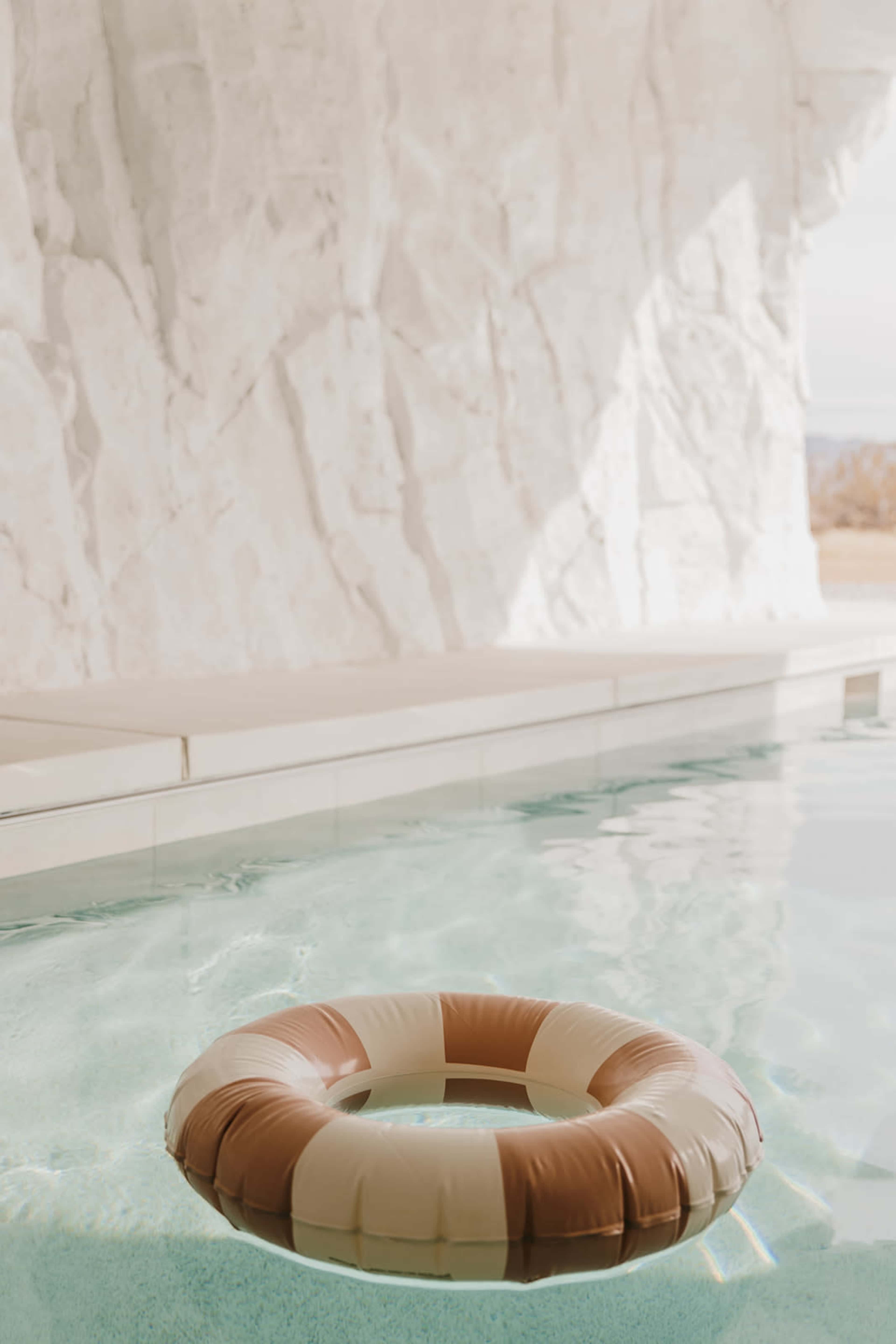 A lifebuoy floats in a clear swimming pool beside a white rock wall.