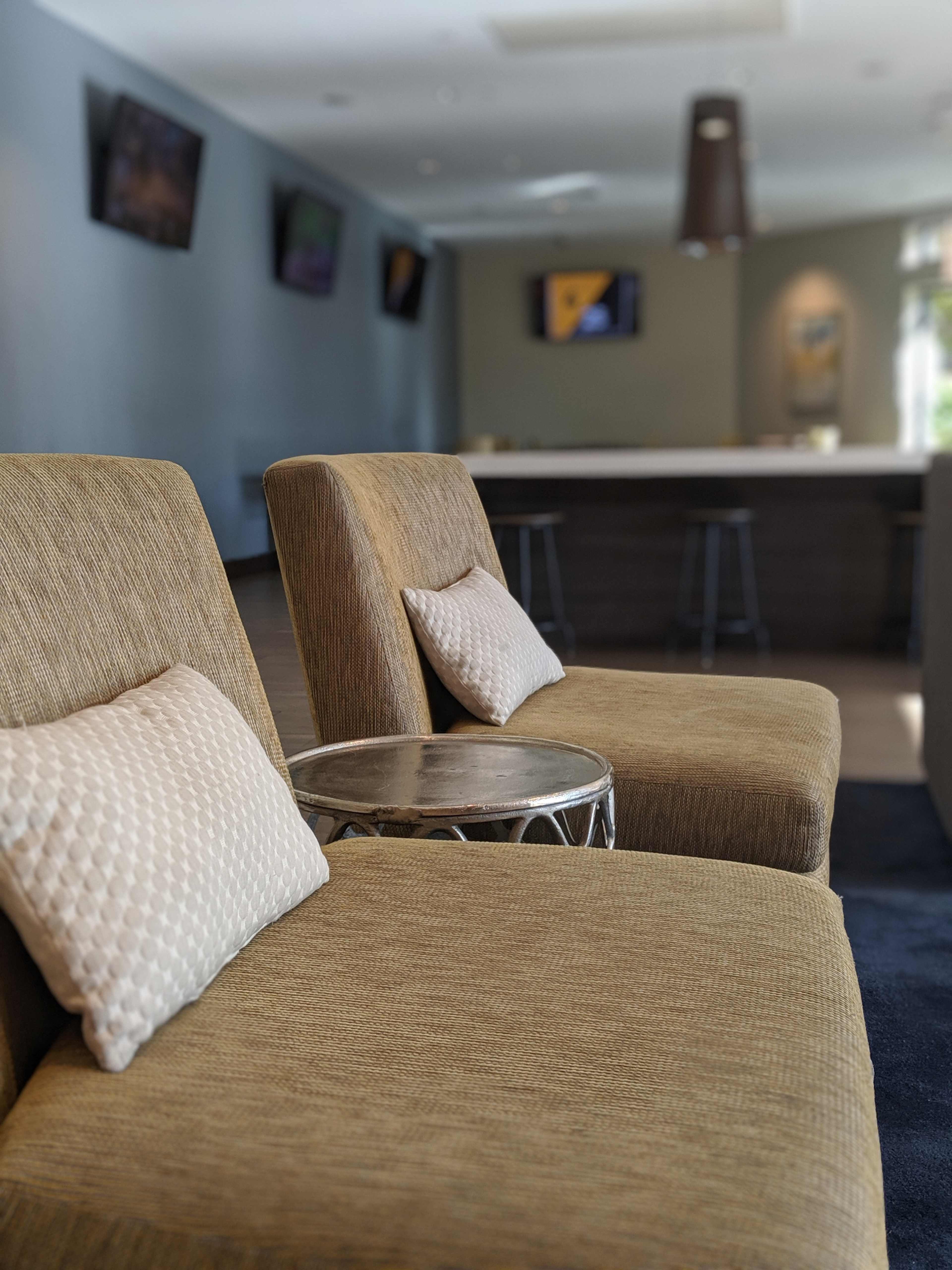 Two modern chairs with cushions beside a small circular table in a lounge area that features a bar in the background.