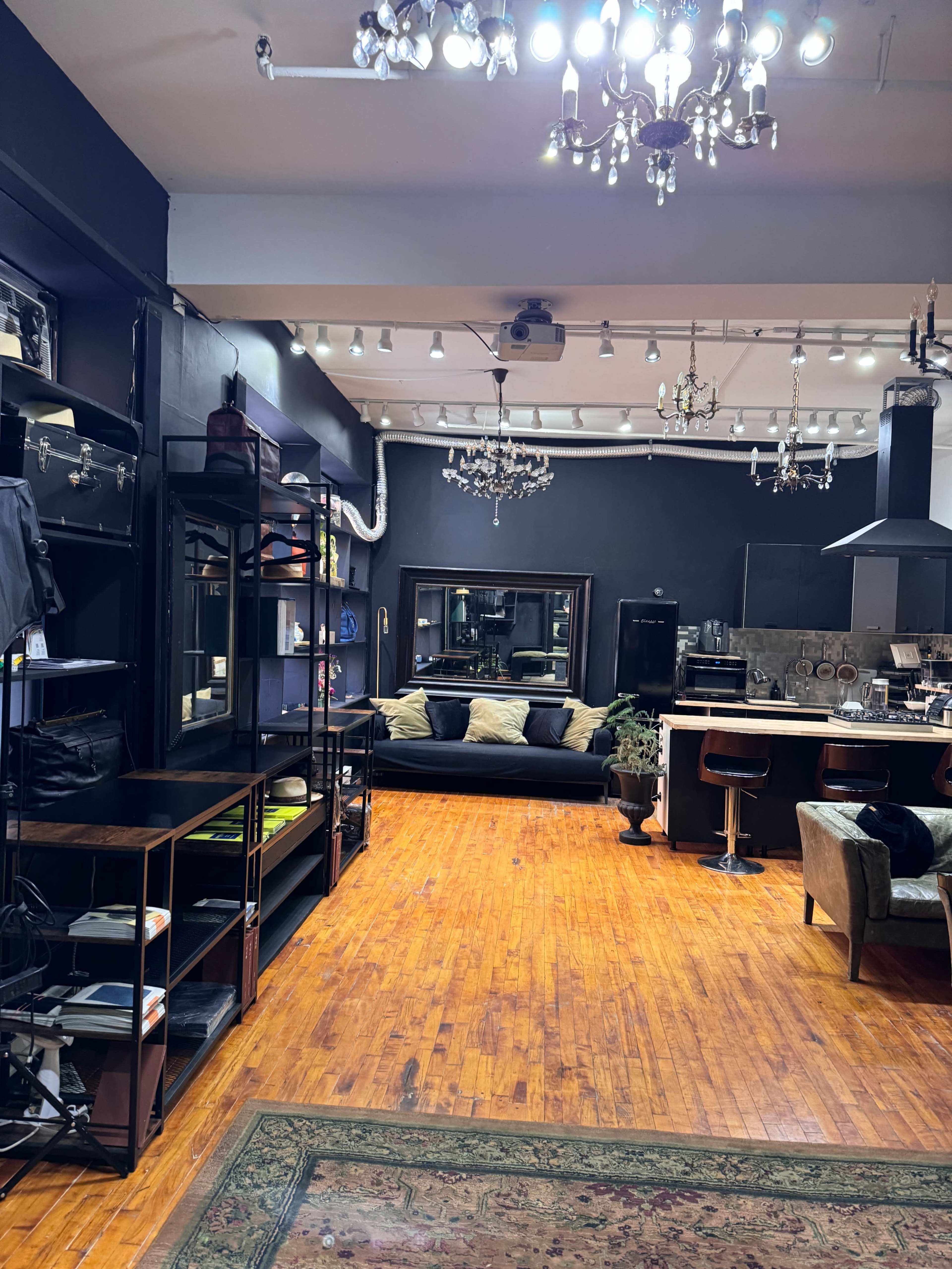 A modern retail space featuring wooden floors, black walls, stylish shelving units, a sofa, and a bar area with stools.