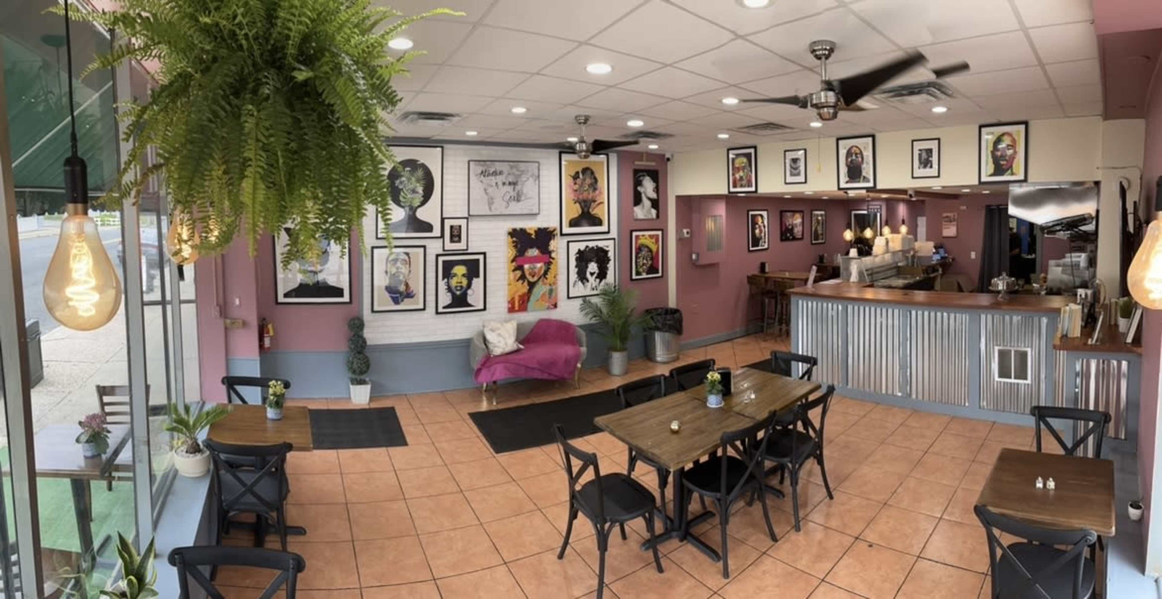 A modern cafe interior with a seating area featuring tables and chairs, colorful wall art, and a counter with a coffee bar.
