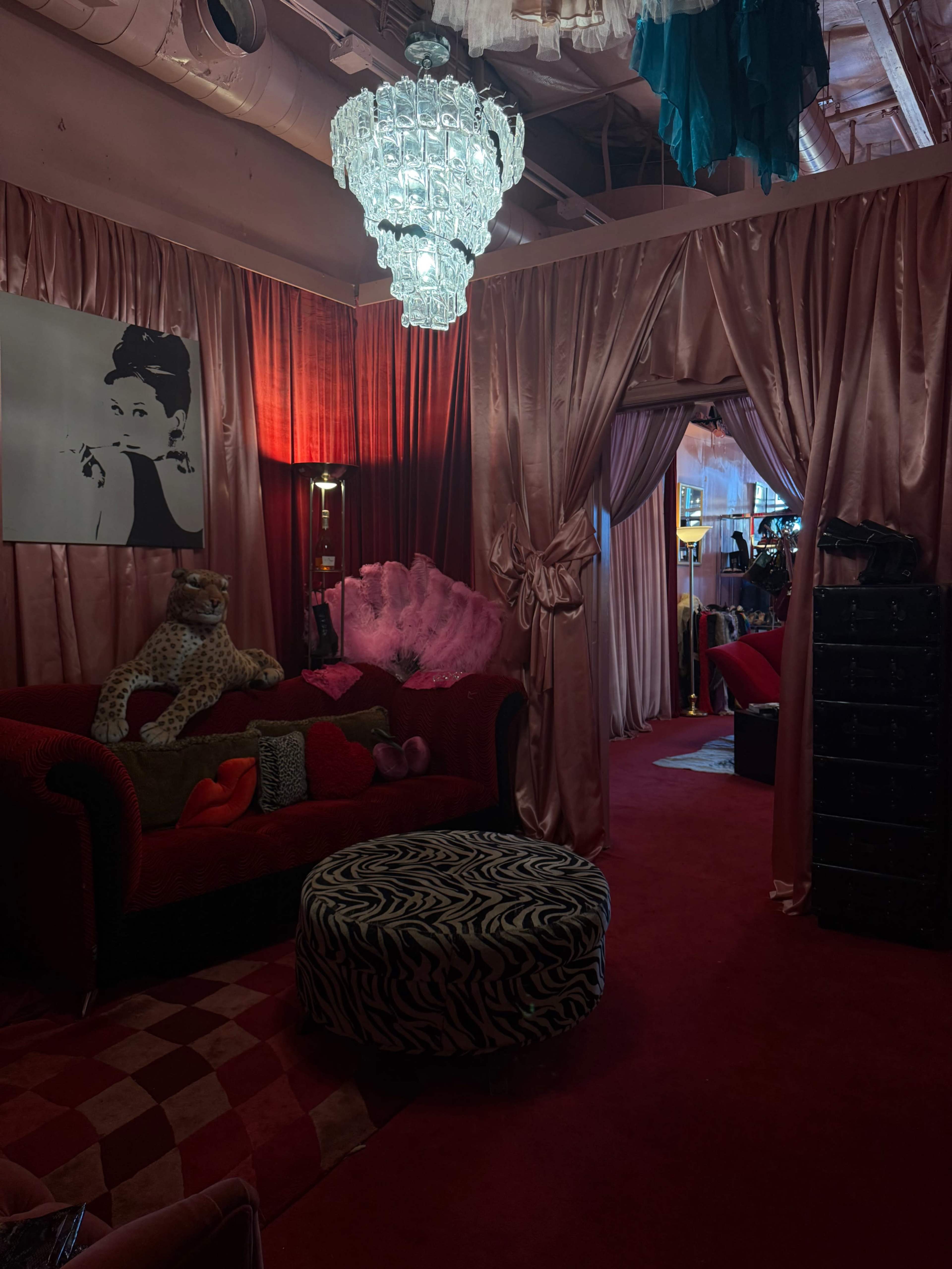The image shows a stylishly decorated room with plush furniture, draped curtains, and a large chandelier, featuring a black and white portrait of a woman on the wall.