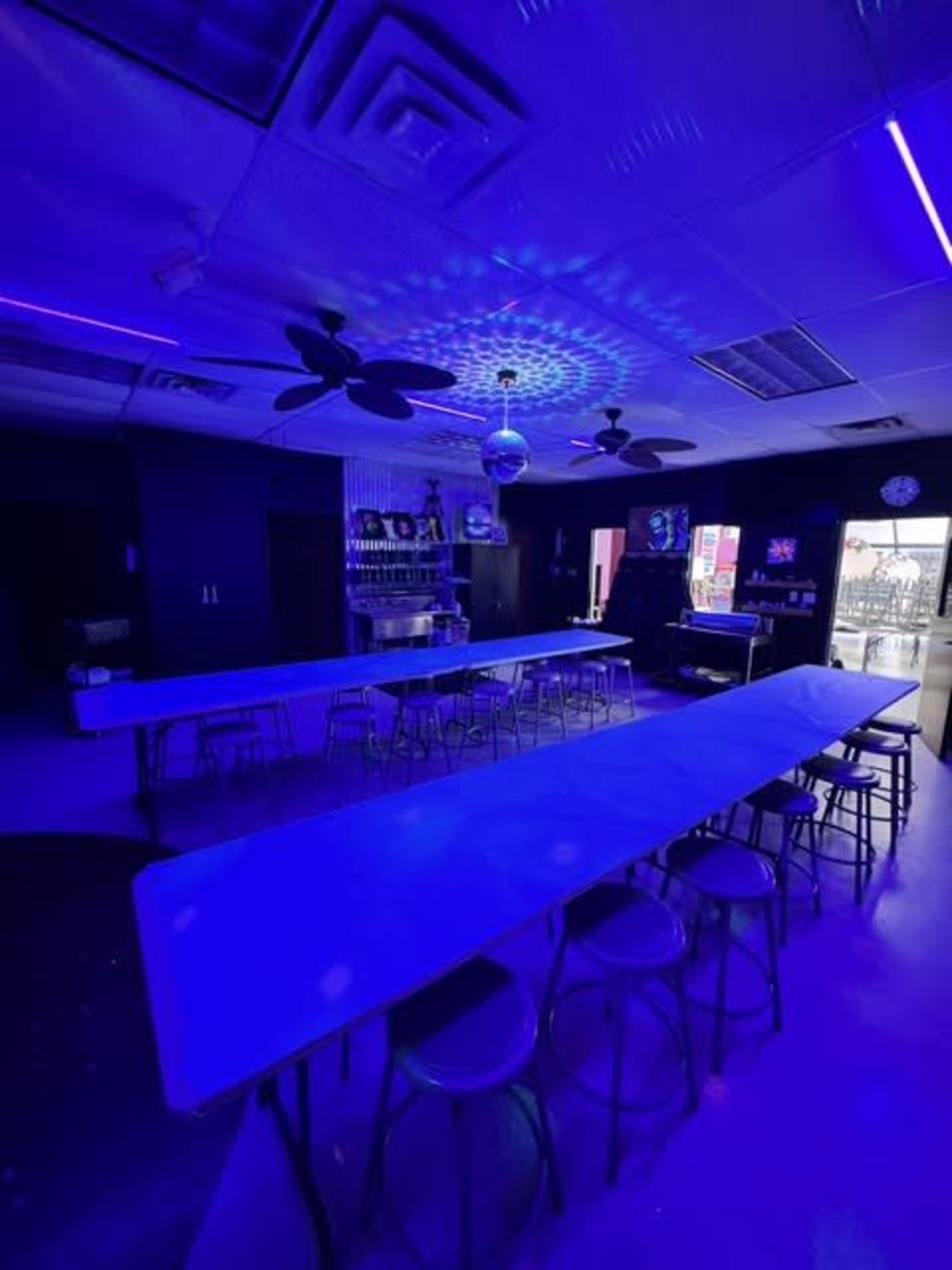 An interior space features blue lighting, long tables, and a disco ball hanging from the ceiling.