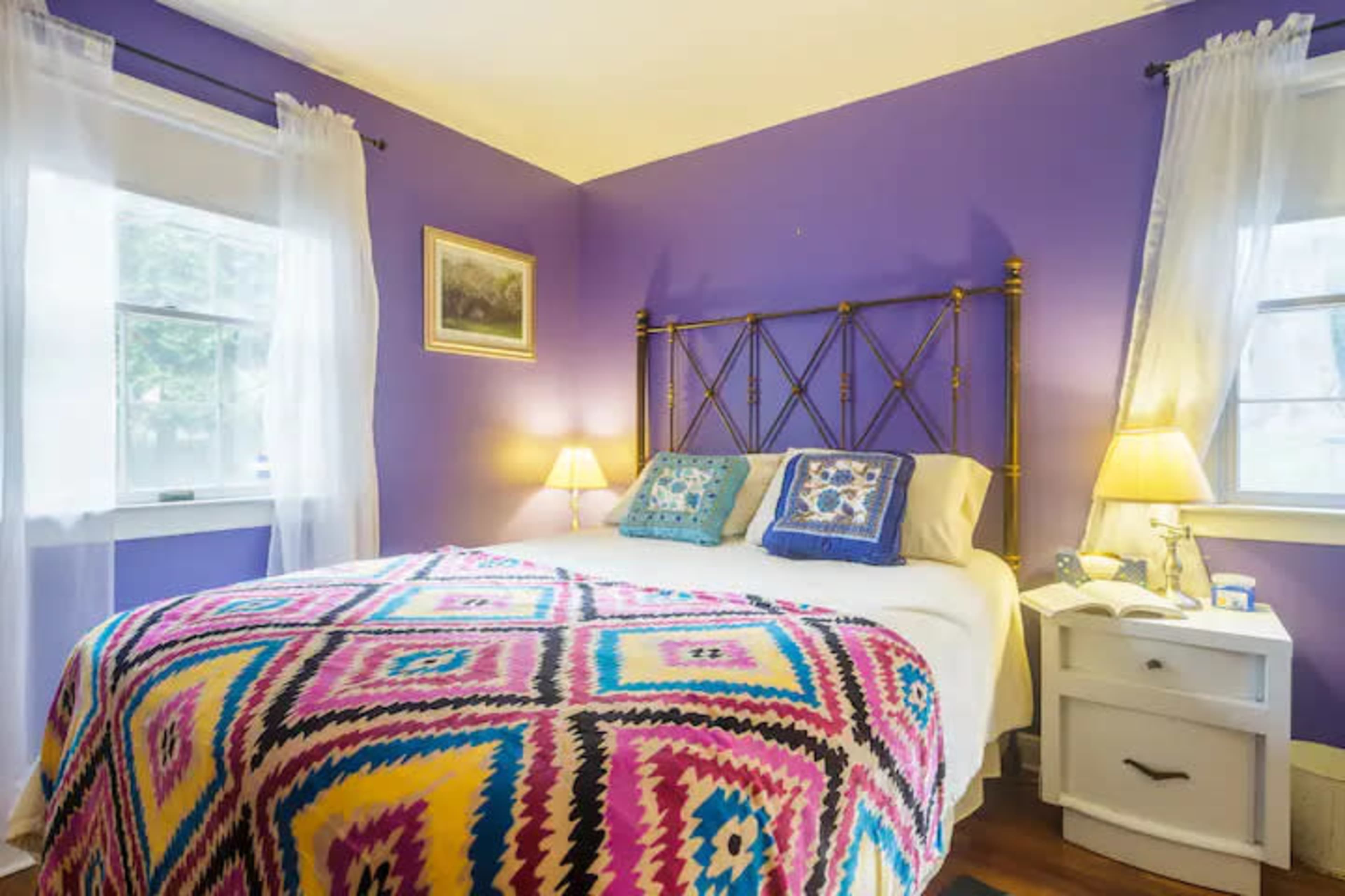 A bedroom with purple walls, a bed covered in a colorful blanket, and two bedside lamps illuminating the space.