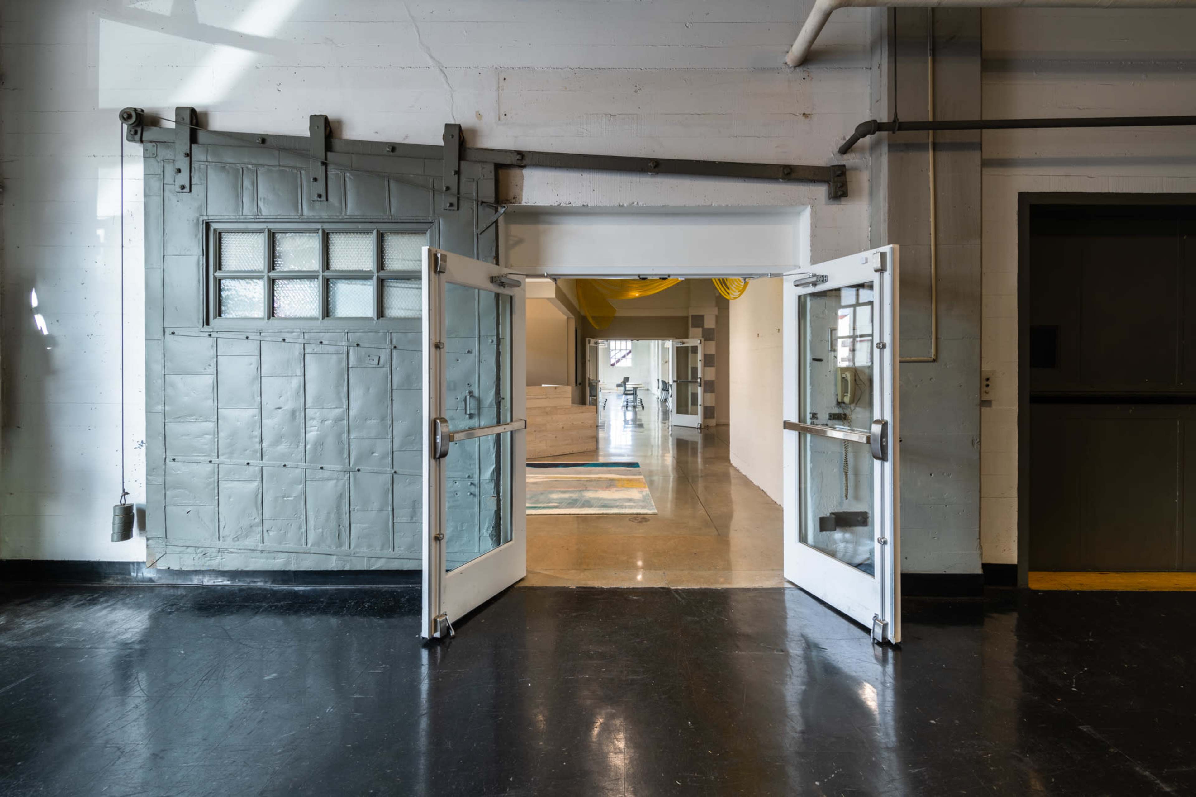 A spacious interior with double doors opening into a well-lit area featuring polished concrete floors and minimalist decor.