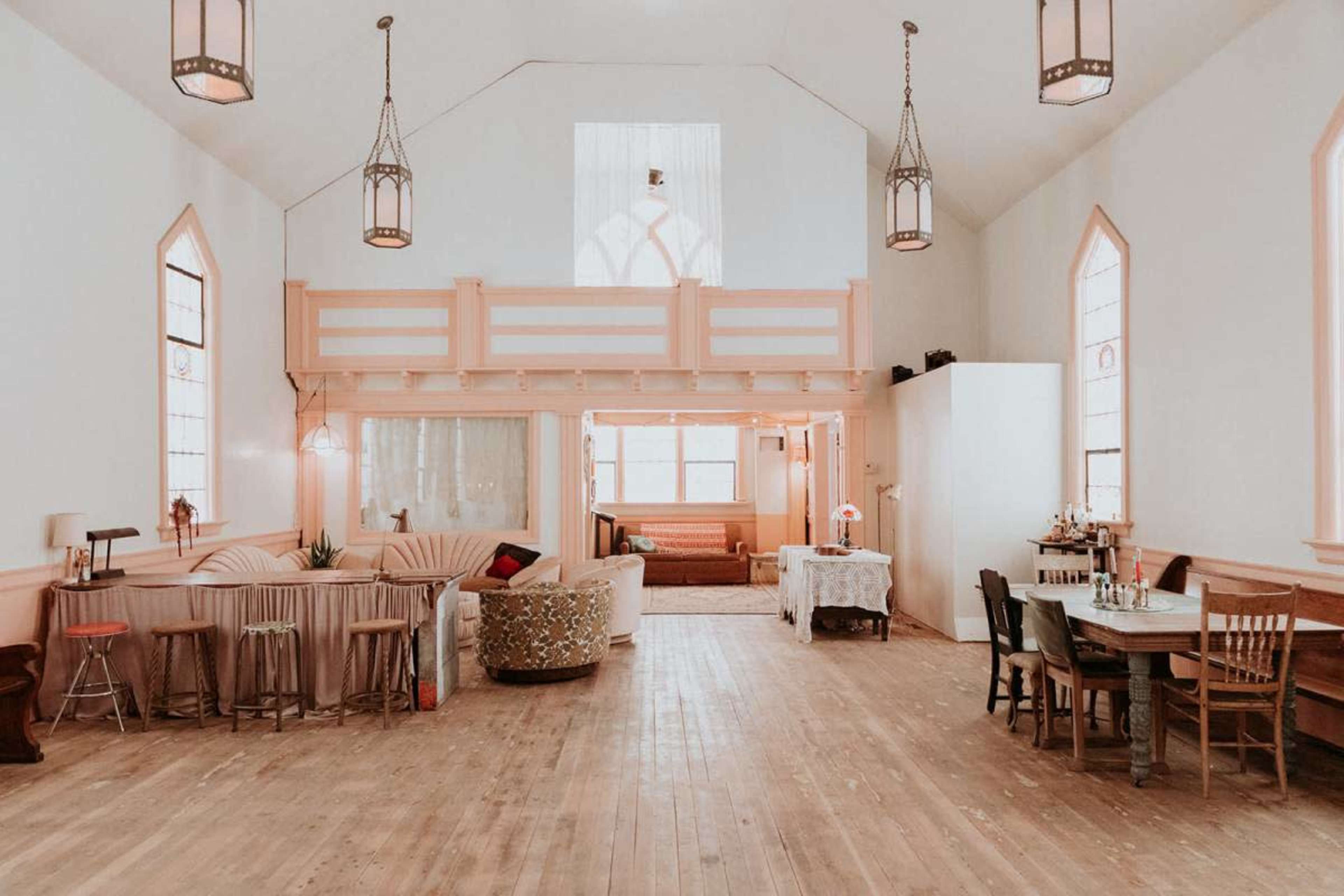 The image shows a spacious, modern interior of a renovated building with wooden floors, large windows, and a mixture of seating areas and dining spaces.
