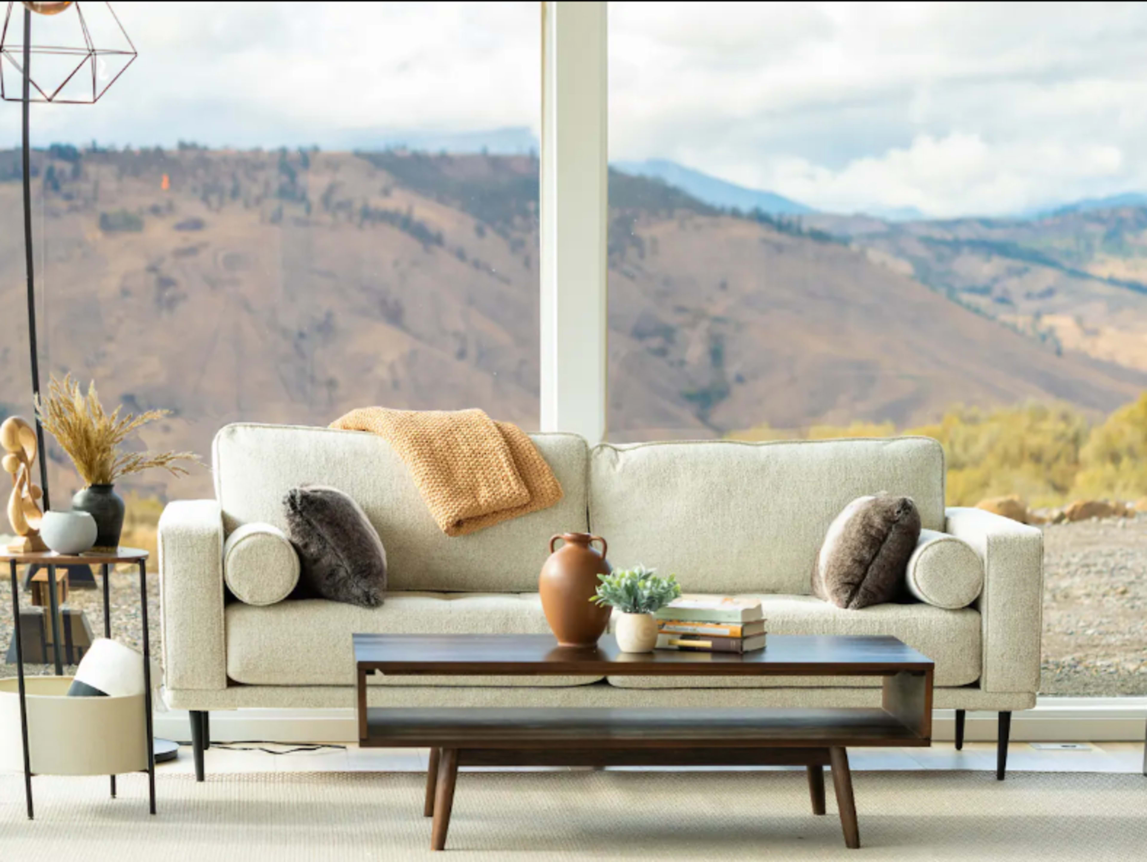 A light-colored sofa with decorative pillows sits in front of a large window showcasing a mountainous landscape.