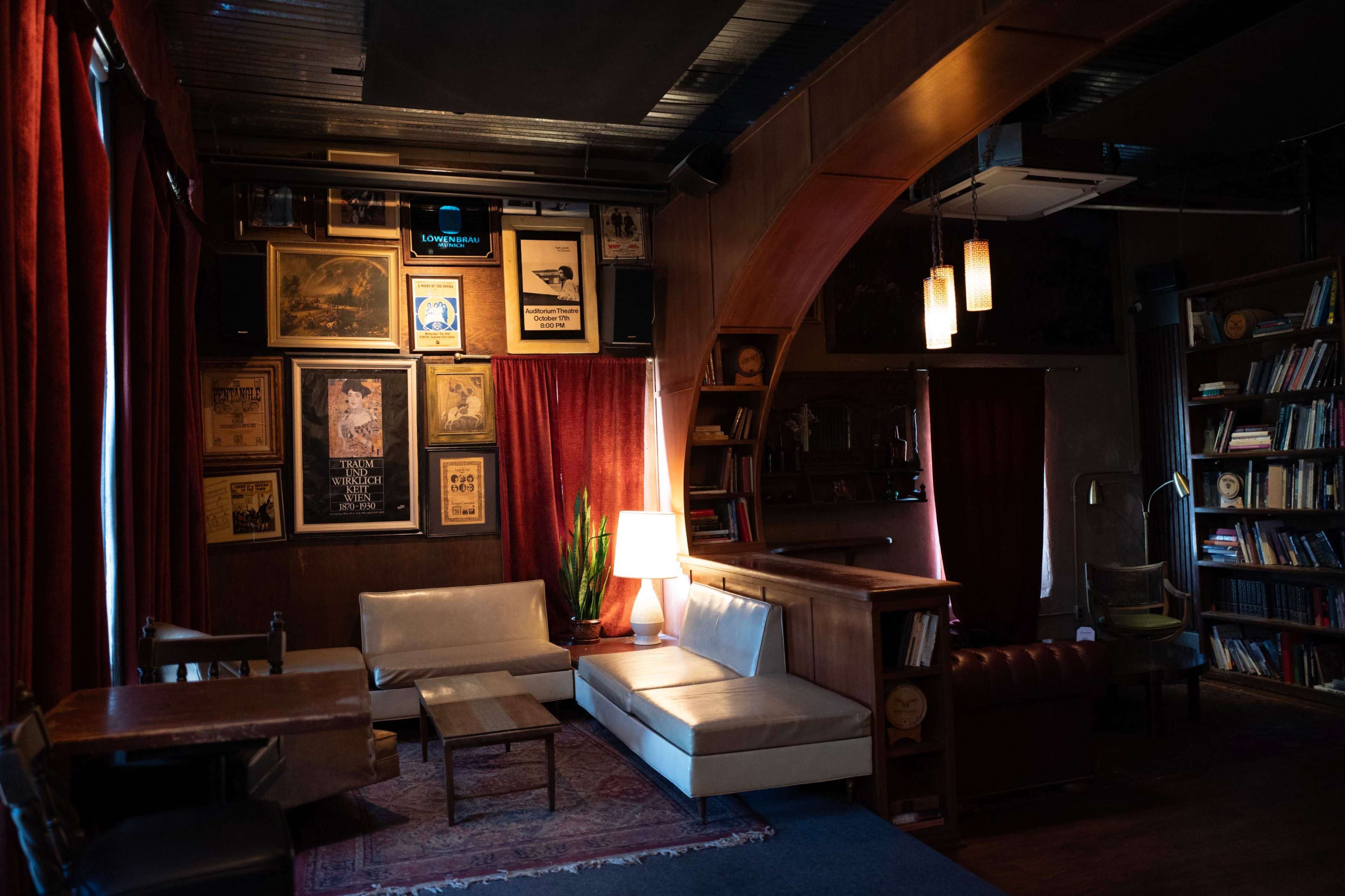 The image shows a cozy lounge area in a dimly lit room, featuring a mix of vintage decorations, seating arrangements, and warm lighting.