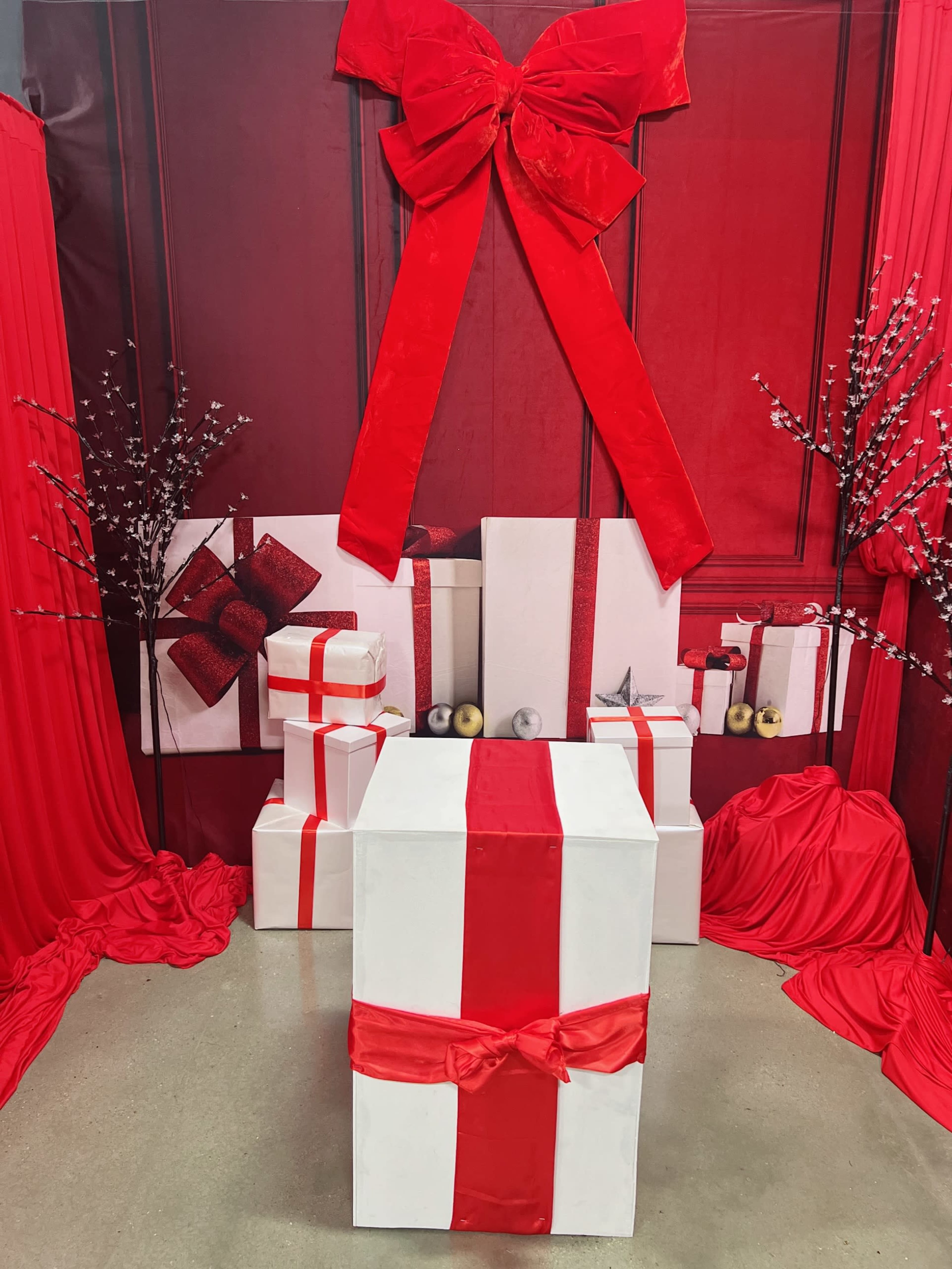The scene features a decorated backdrop with a large red bow, multiple white and red wrapped gift boxes, and red drapery.