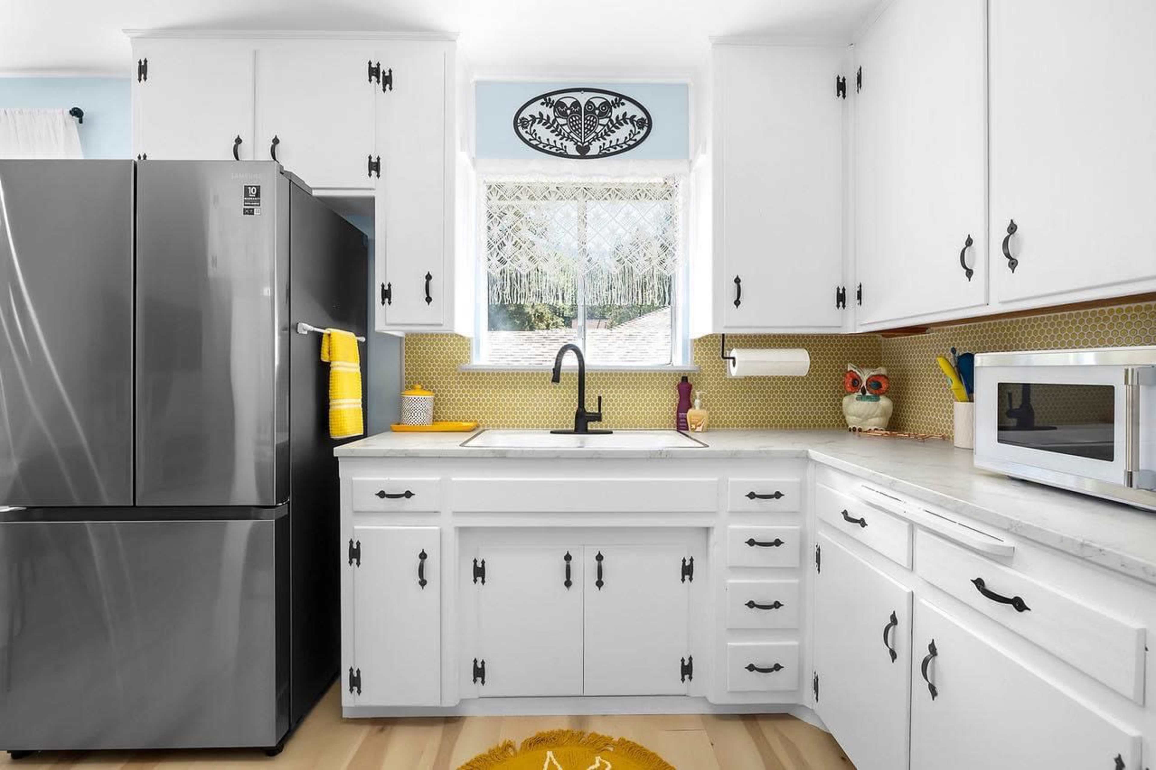 A modern kitchen features white cabinetry, a stainless steel refrigerator, and a window above the sink.