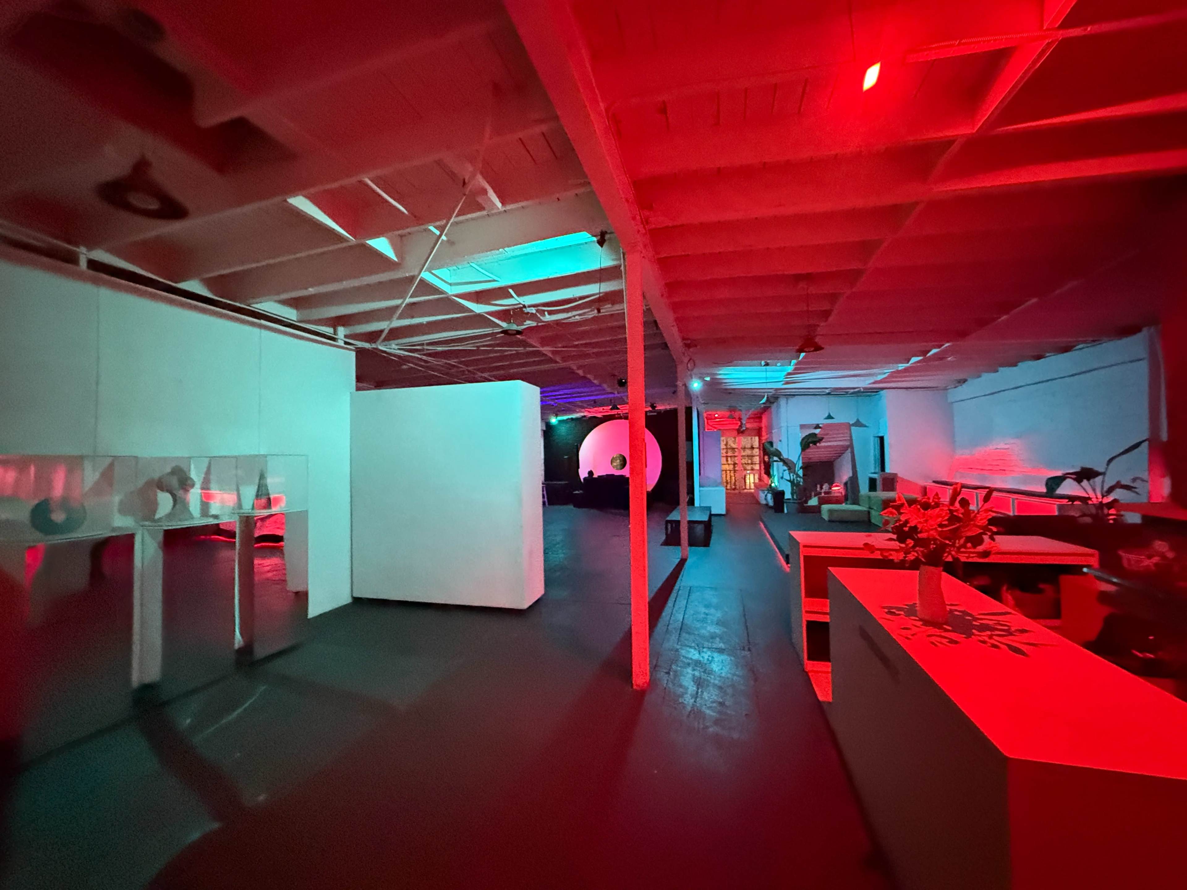 The image shows an industrial-style interior space with a split lighting scheme, featuring vibrant red and blue hues, and minimalistic white structures.