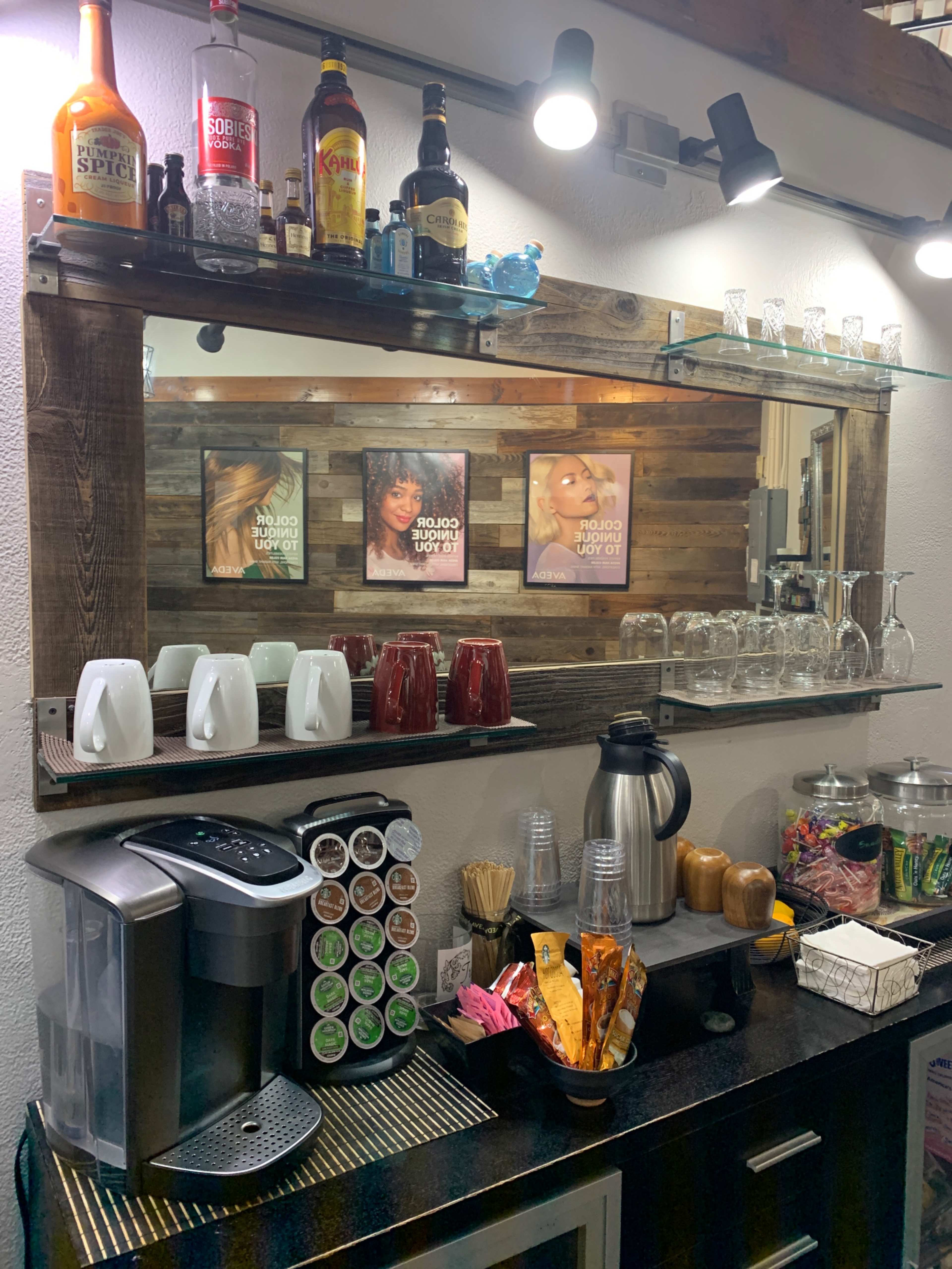 A coffee station is set up against a wooden wall, featuring a variety of beverages, glassware, and decorative framed photos above.