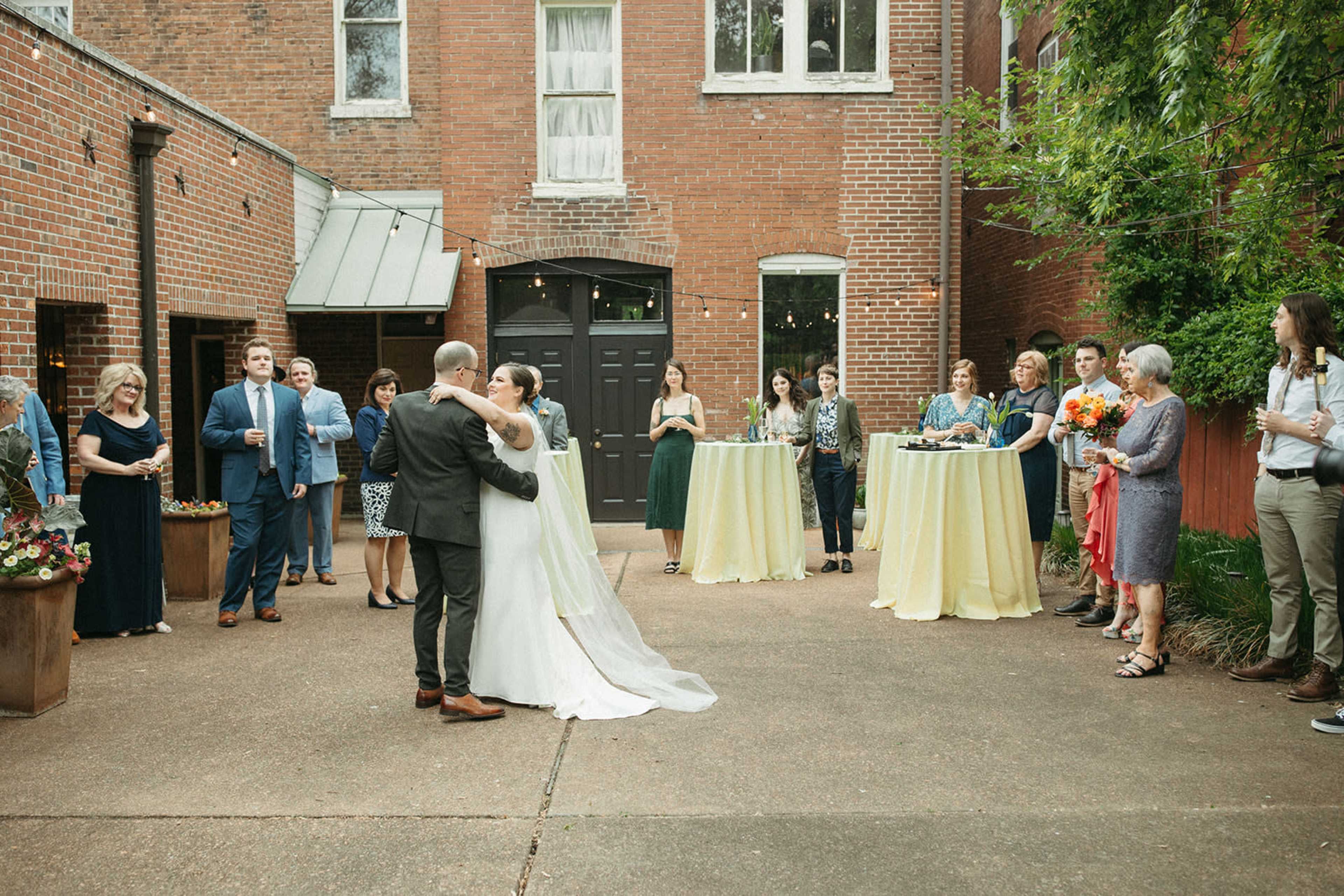 A couple dances together in an outdoor courtyard surrounded by guests during a wedding celebration.
