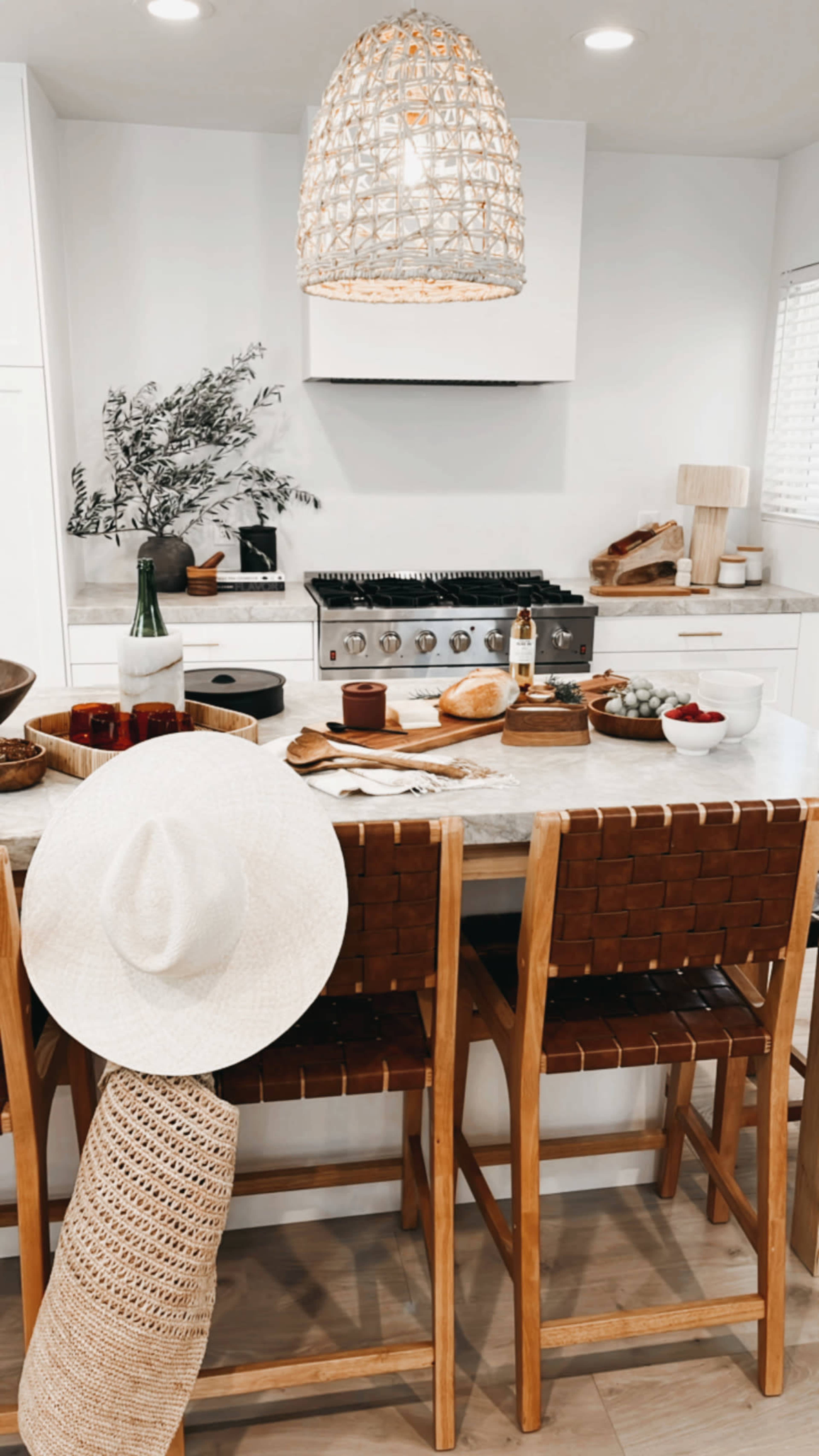The kitchen features a modern design with a large gas stove, wooden bar stools, and a table set with various food items and decorative elements.