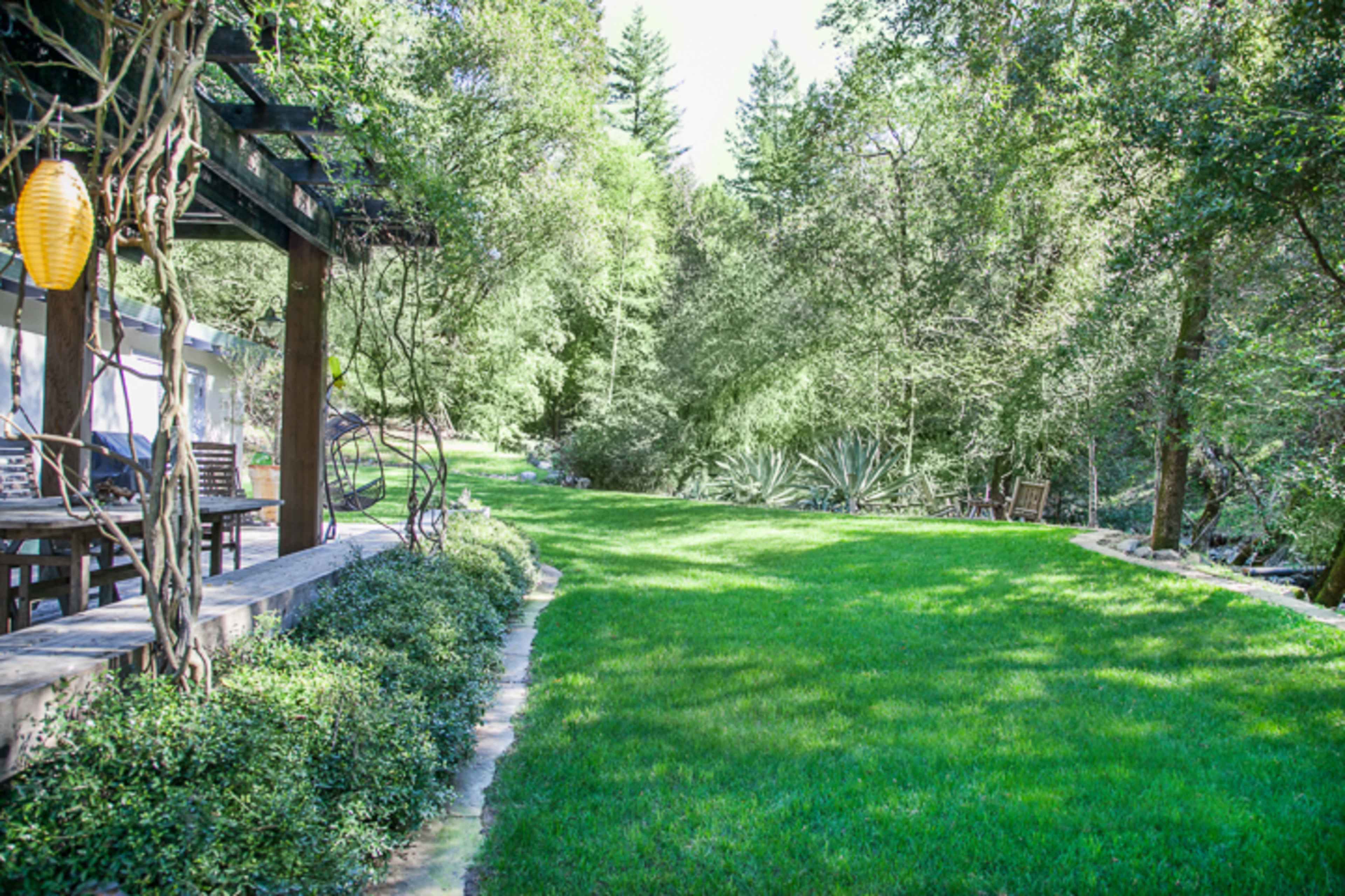 A well-manicured lawn surrounded by trees and shrubs, with a patio area featuring outdoor furniture to the side.