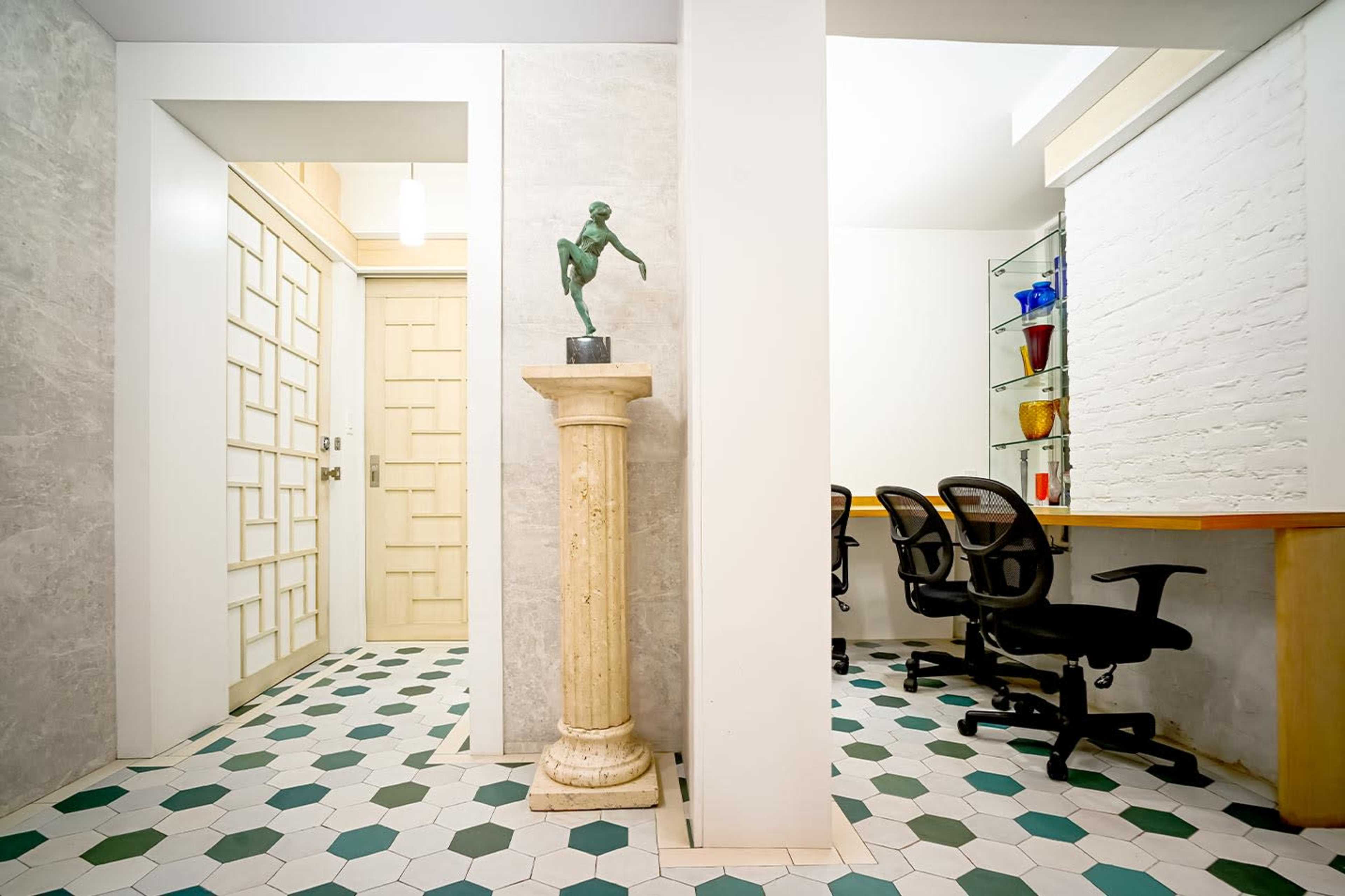 The image shows a modern interior space featuring a sculpture on a pedestal, a geometric tile floor, and a workspace with chairs and shelves.