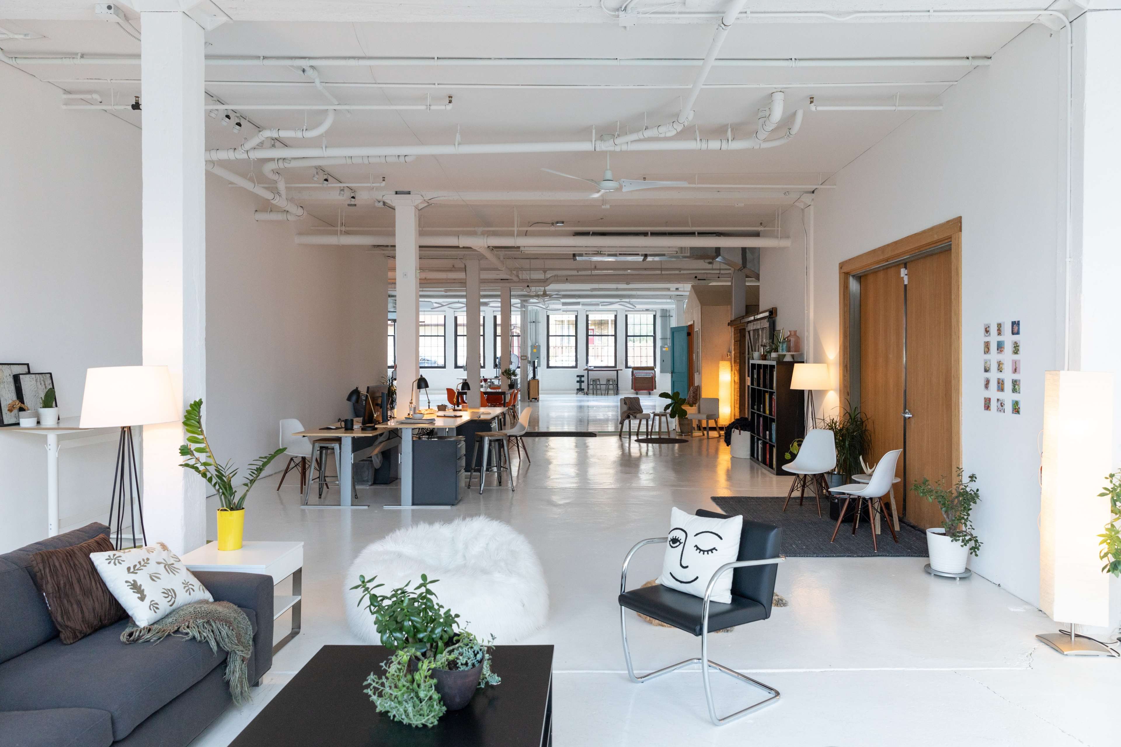 A spacious, modern office area with desks, seating, and plants arranged in a bright, minimally decorated interior.
