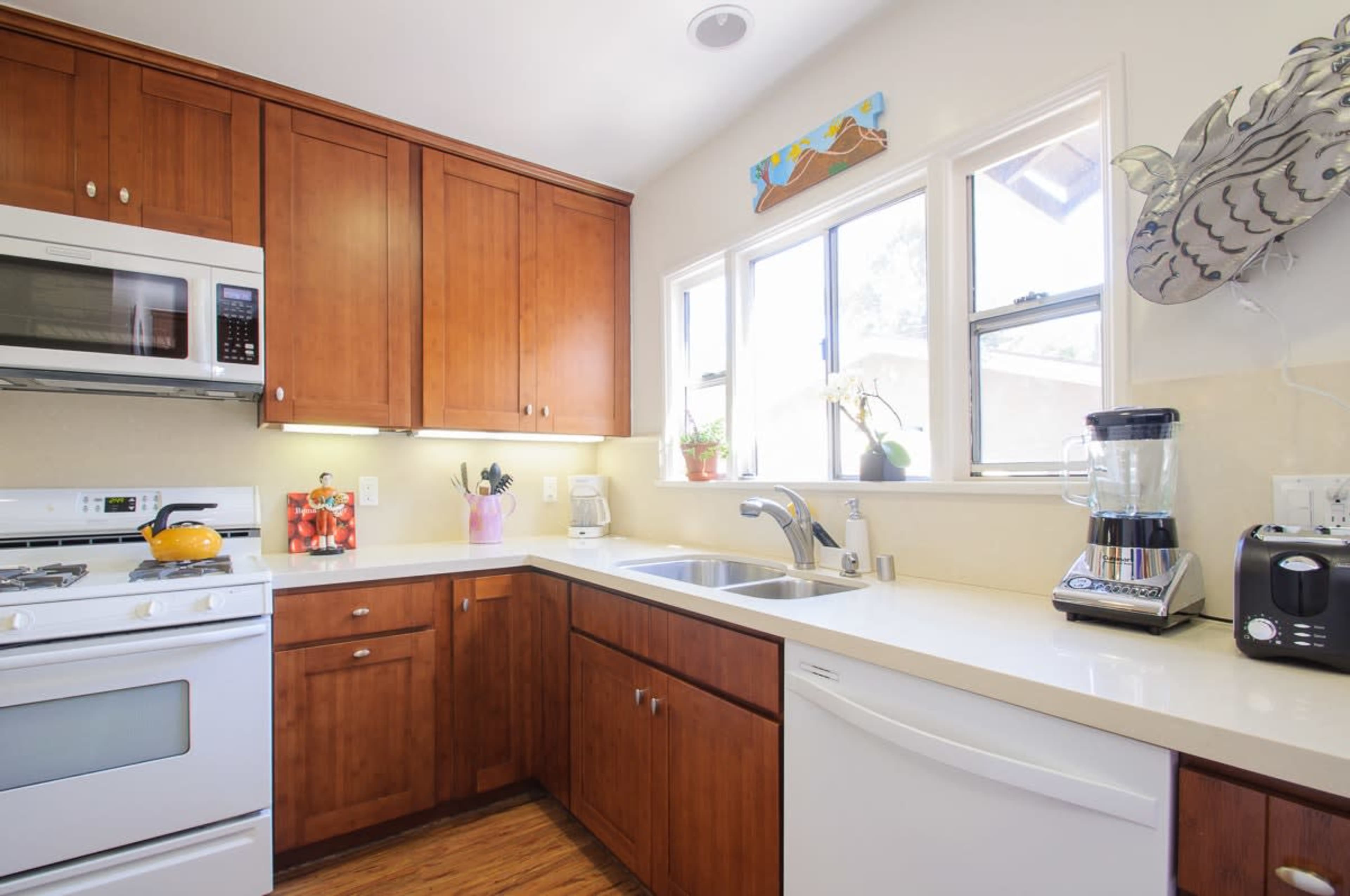 A modern kitchen features wooden cabinets, stainless steel appliances, and a white countertop with a sink and blender.
