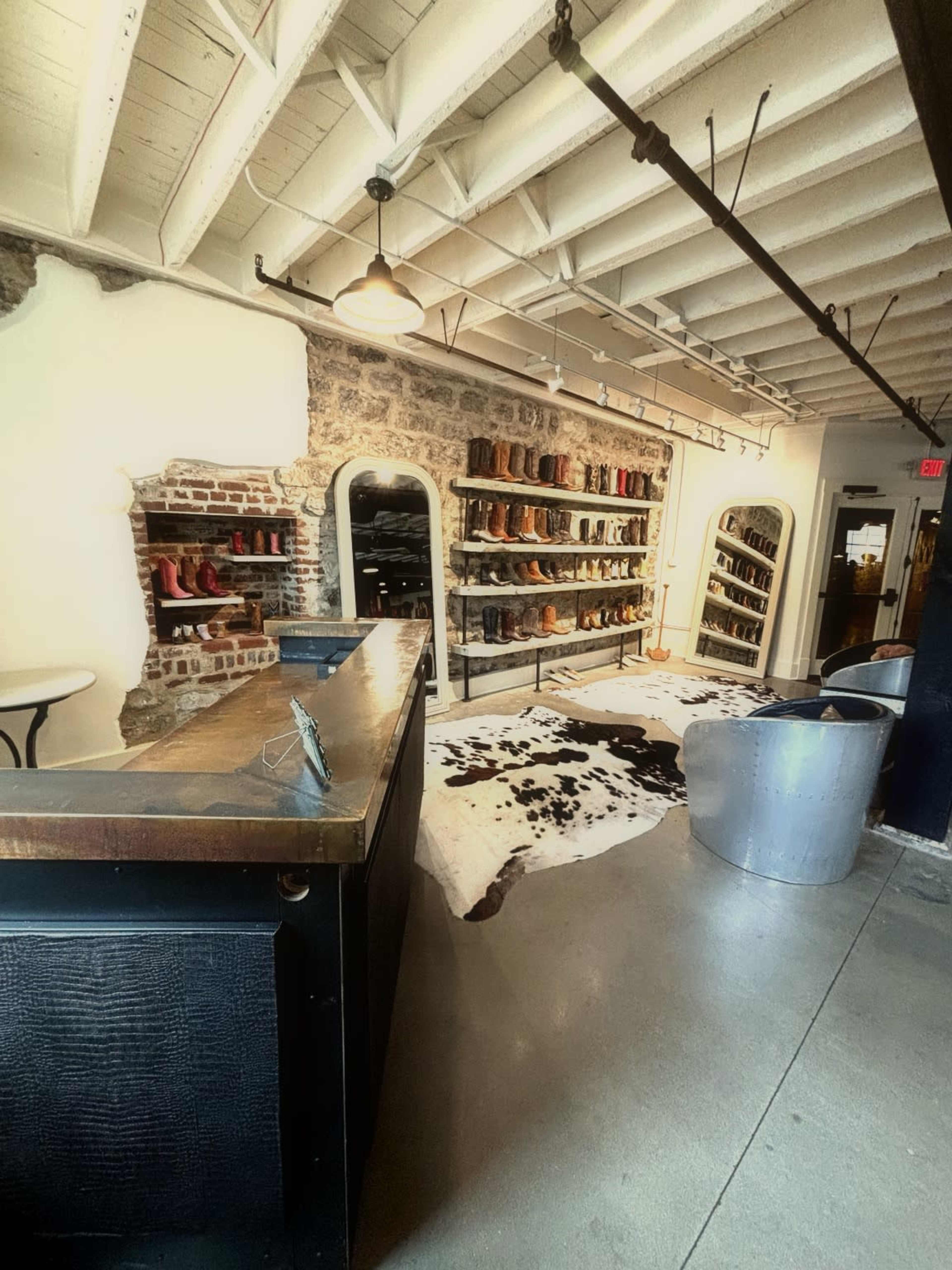 The image shows a rustic shoe store interior with a display of boots on shelves and a cowhide rug on the floor.