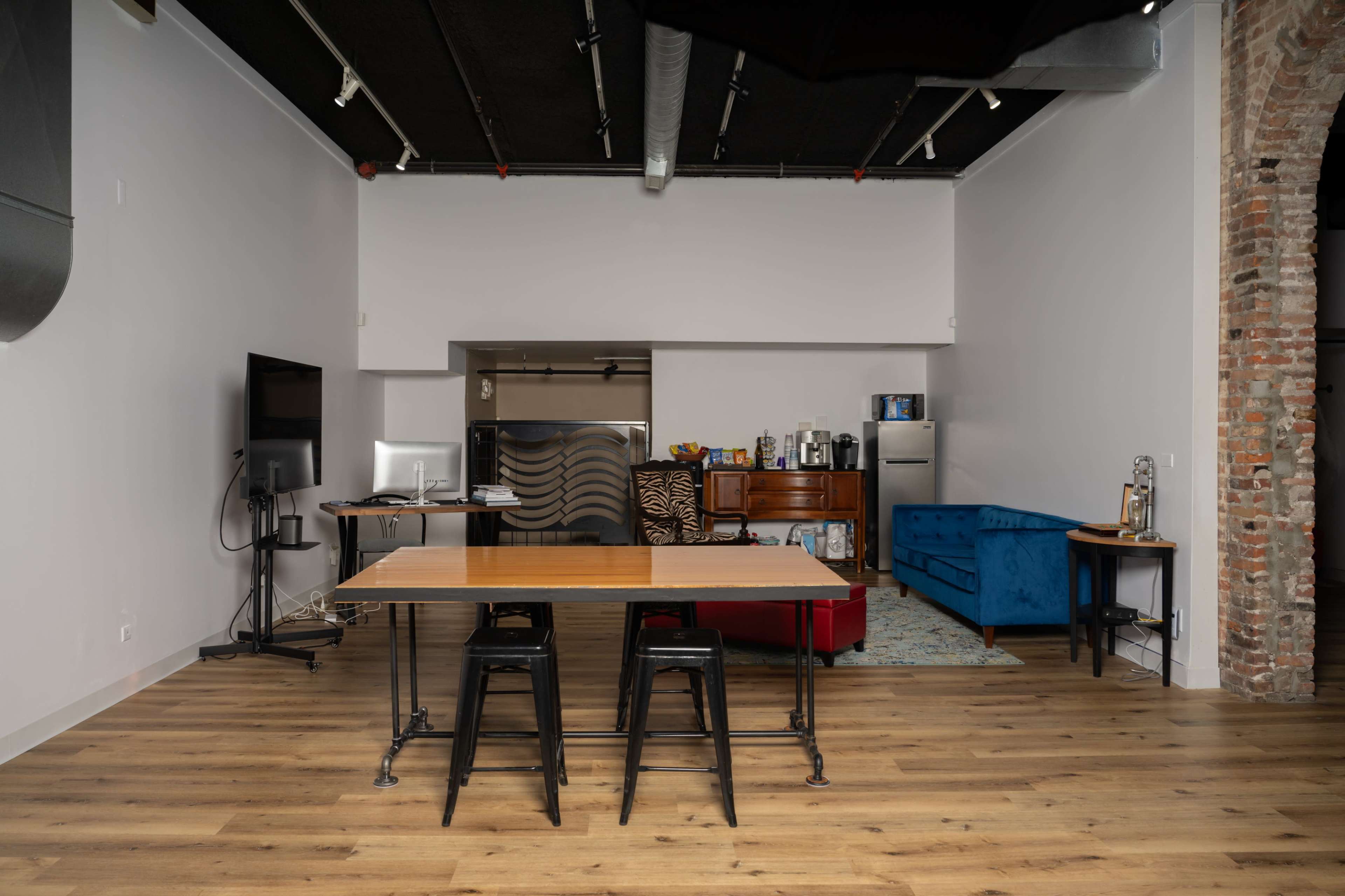 A modern kitchen and living area featuring a dining table with black stools, a blue couch, and various appliances along the walls.