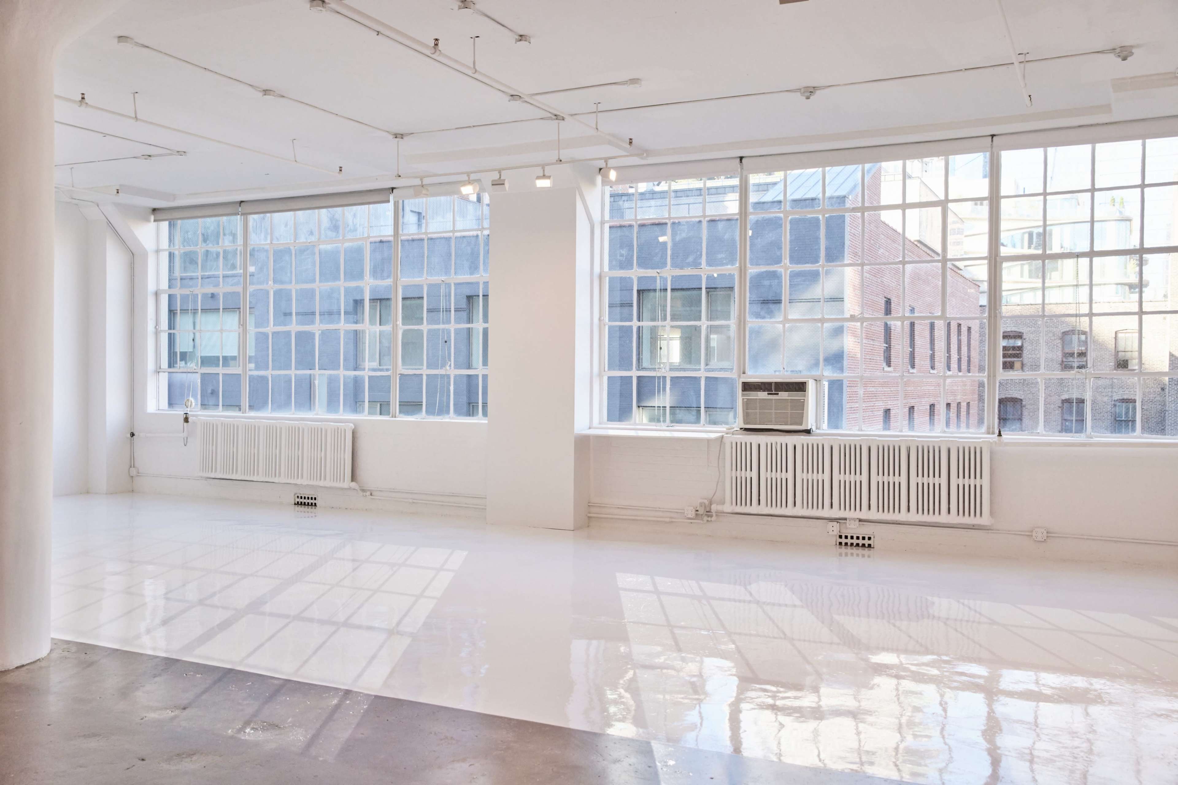 A spacious interior room with large windows, white walls, and a polished floor reflecting light.