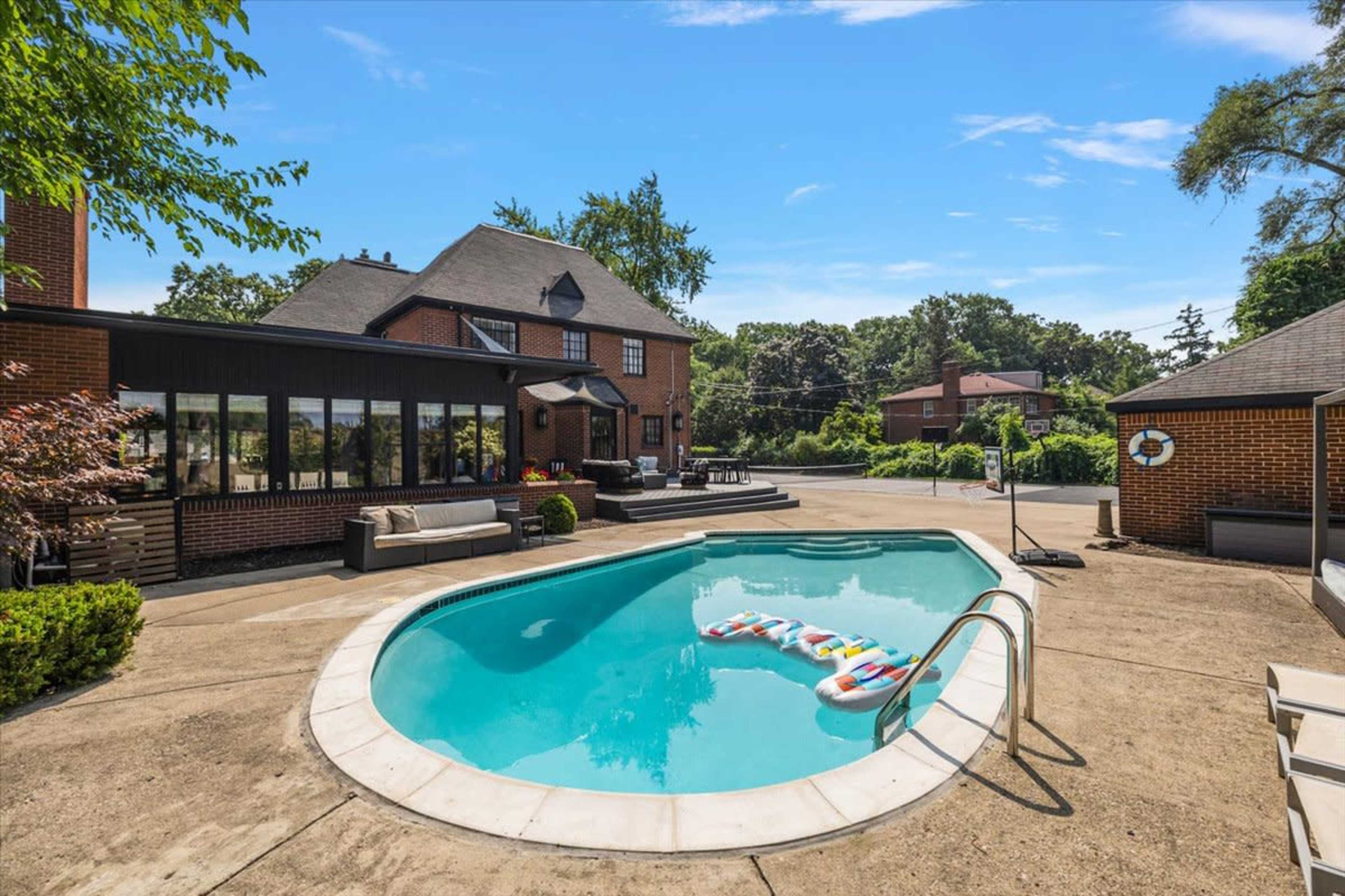 The image shows a backyard pool area with a round swimming pool, surrounding lounge chairs, and a brick house in the background.