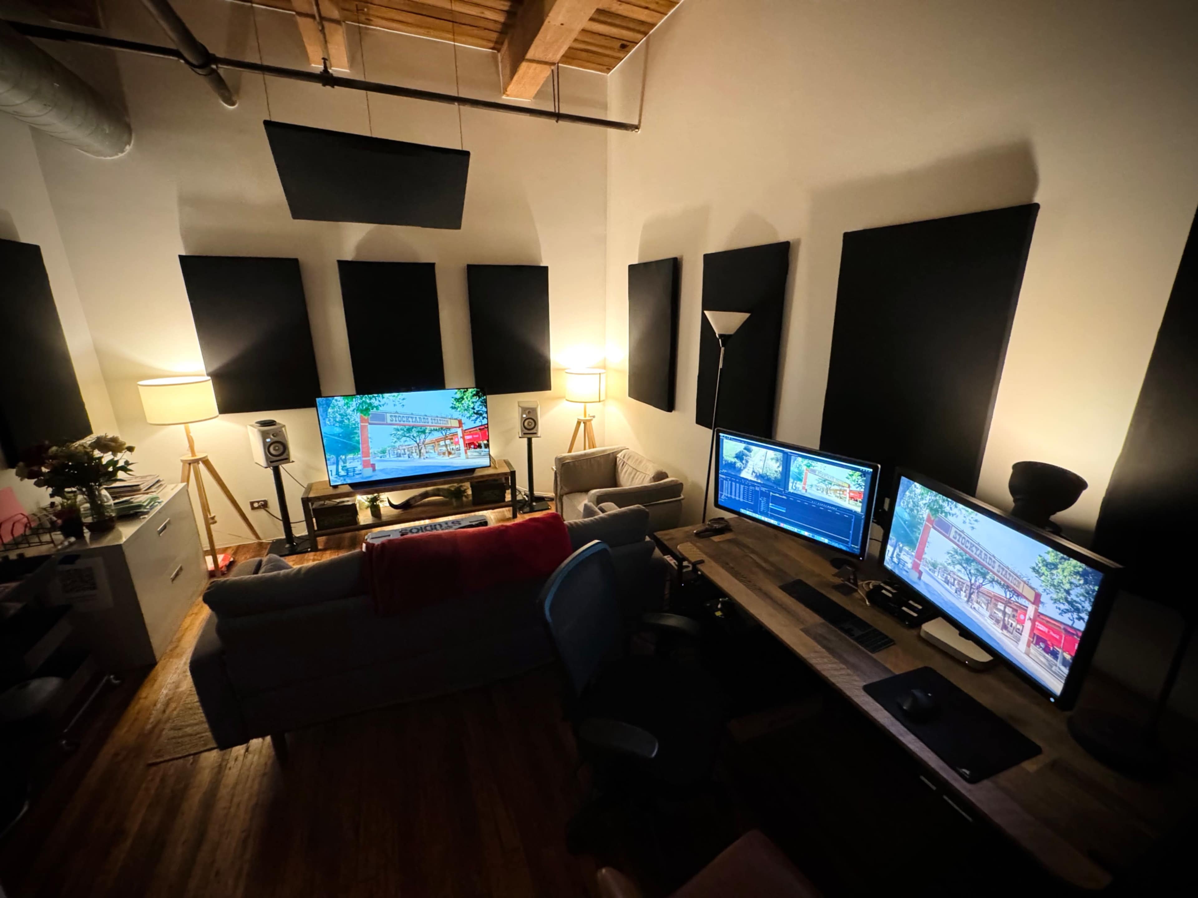 The image shows a modern editing studio with two computer monitors, a large screen, seating, and soundproofing panels on the walls.