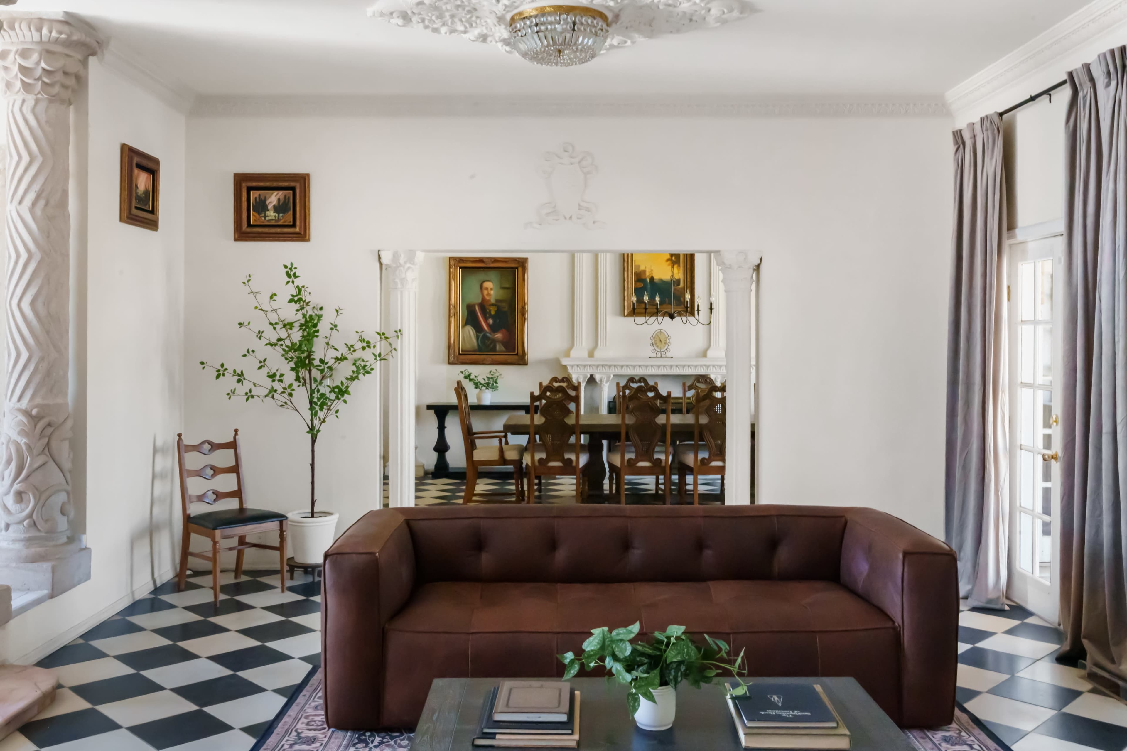 A brown leather sofa is positioned in a spacious living room with black and white checkered flooring, featuring a dining area visible through a large mirror.