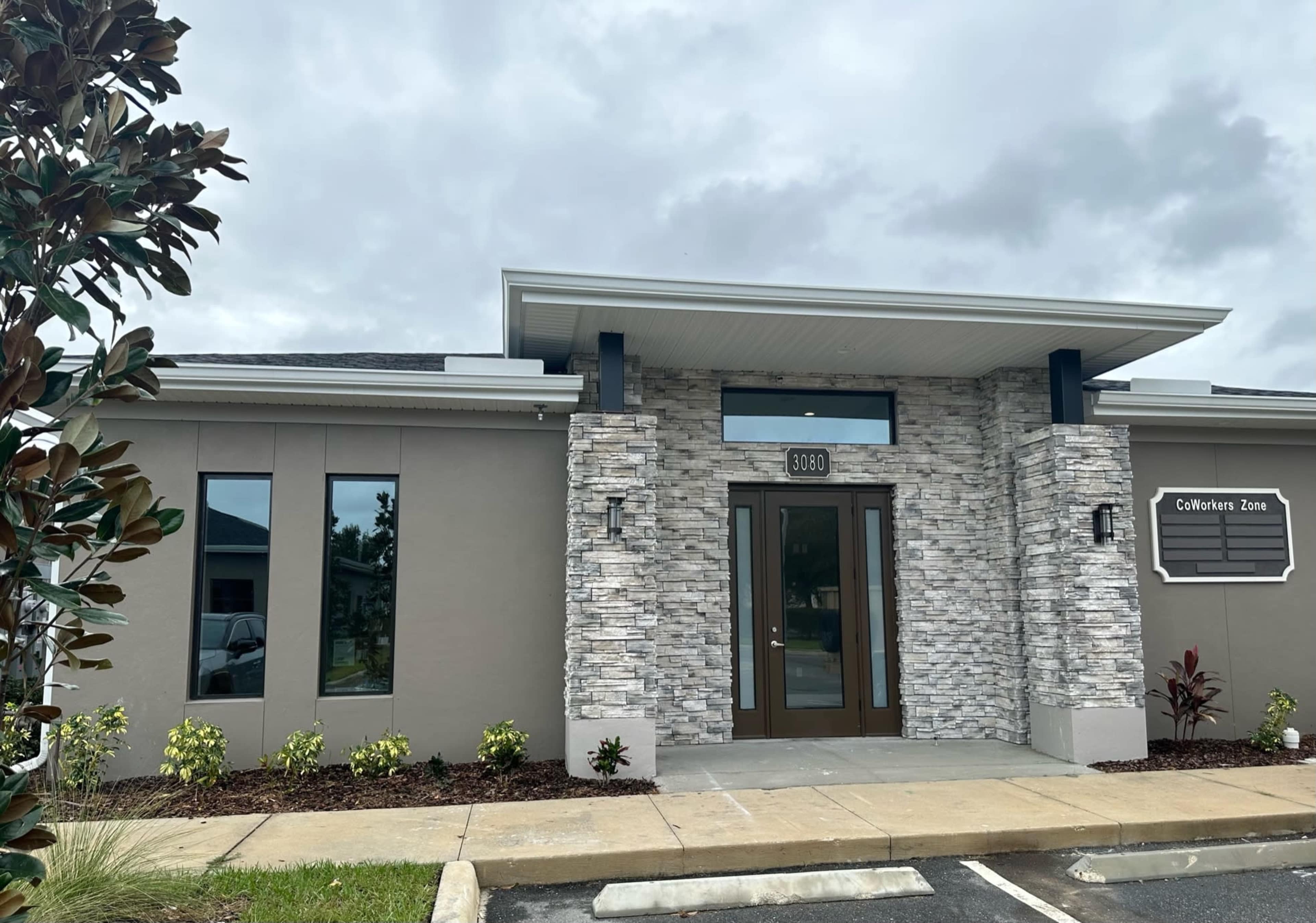 A modern building facade with a stone accent wall, a flat roof, and a prominent entrance labeled "CoWork Zone."