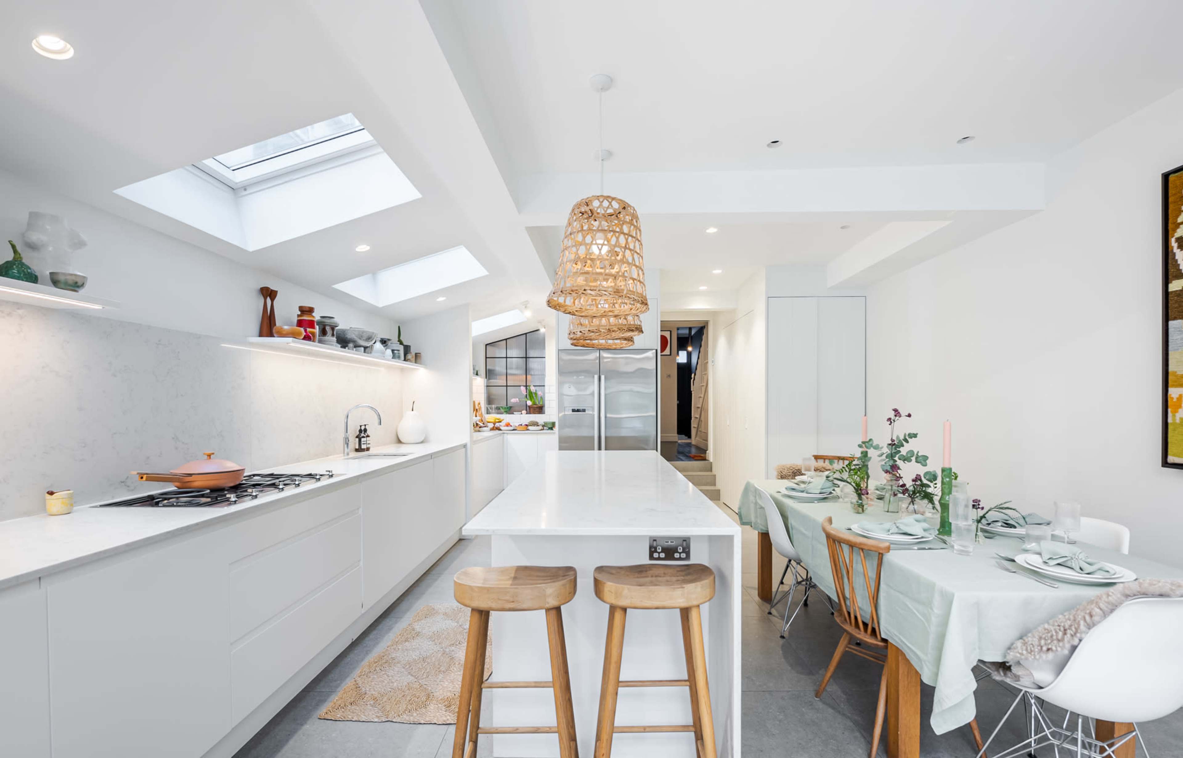 A modern kitchen with a central island, woven pendant light, and an adjacent dining area set with light-colored tableware.