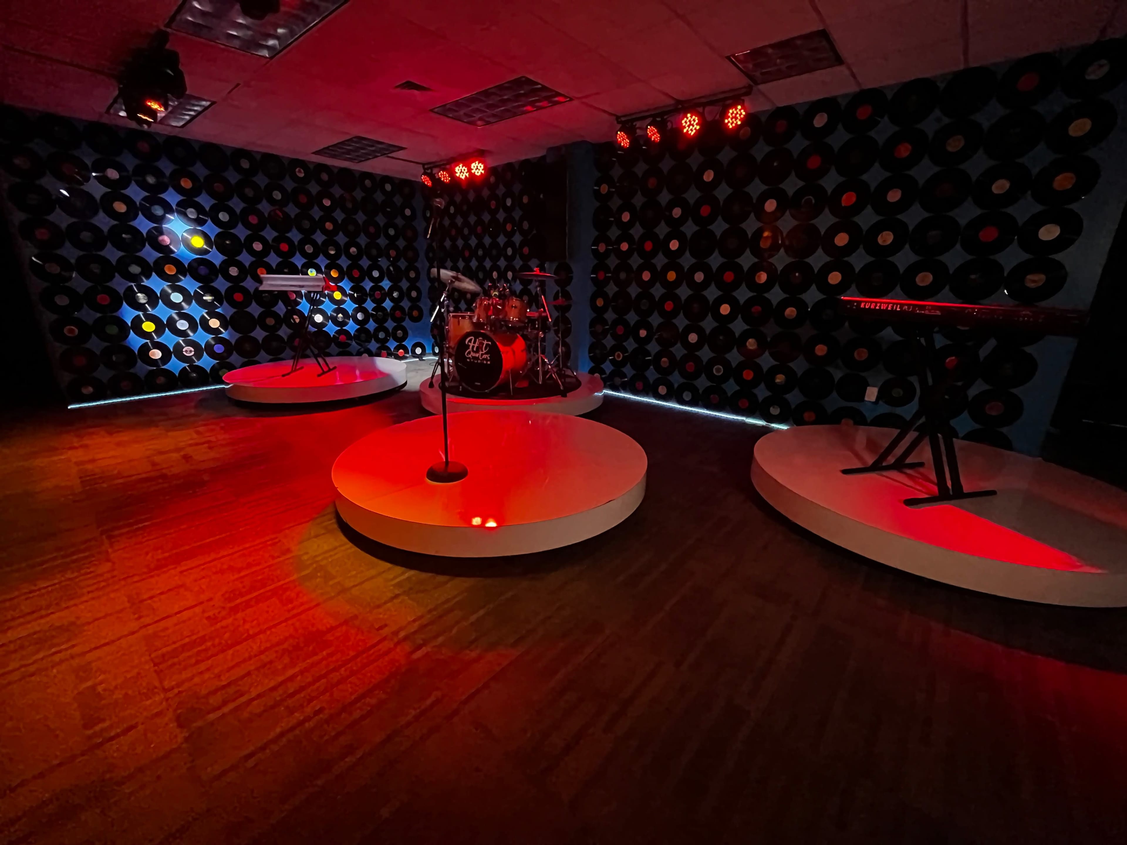 The scene features a music performance space with circular platforms for instruments and a wall decorated with vinyl records, illuminated by red stage lights.