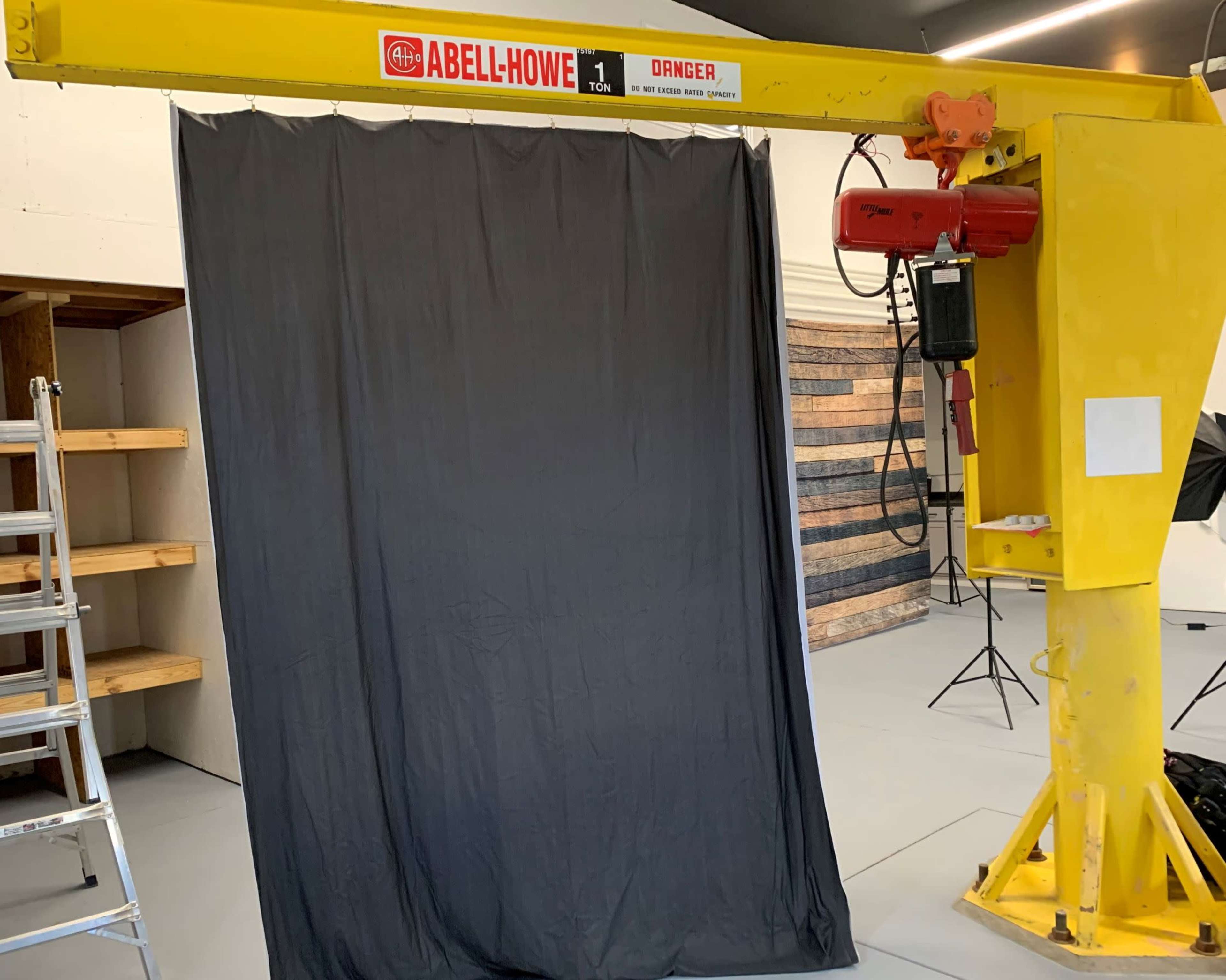 A yellow crane with a hoist is positioned next to a black curtain in an indoor space.