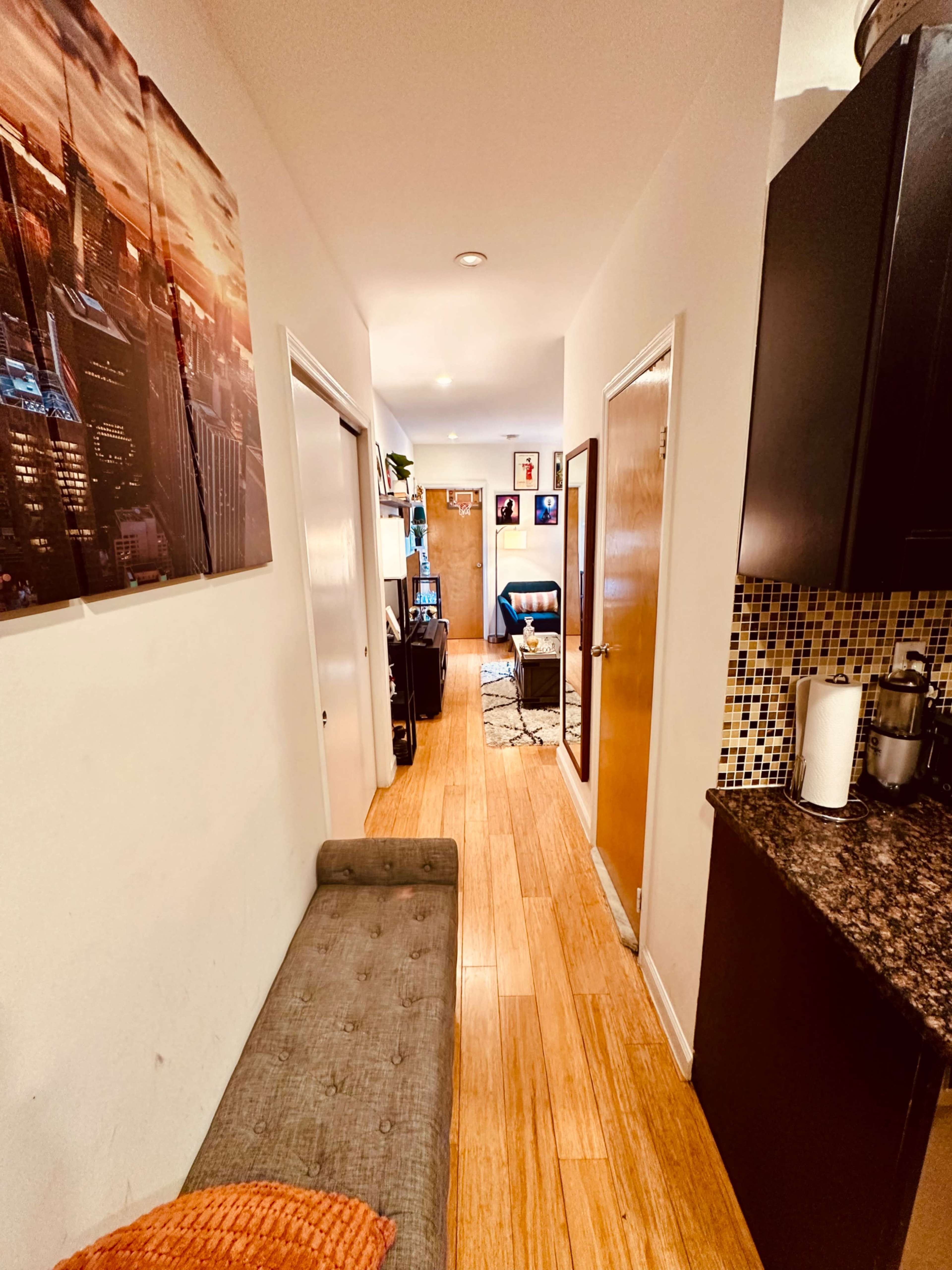 A narrow hallway leading to a living space, with doors on either side and a decorative canvas on the wall.
