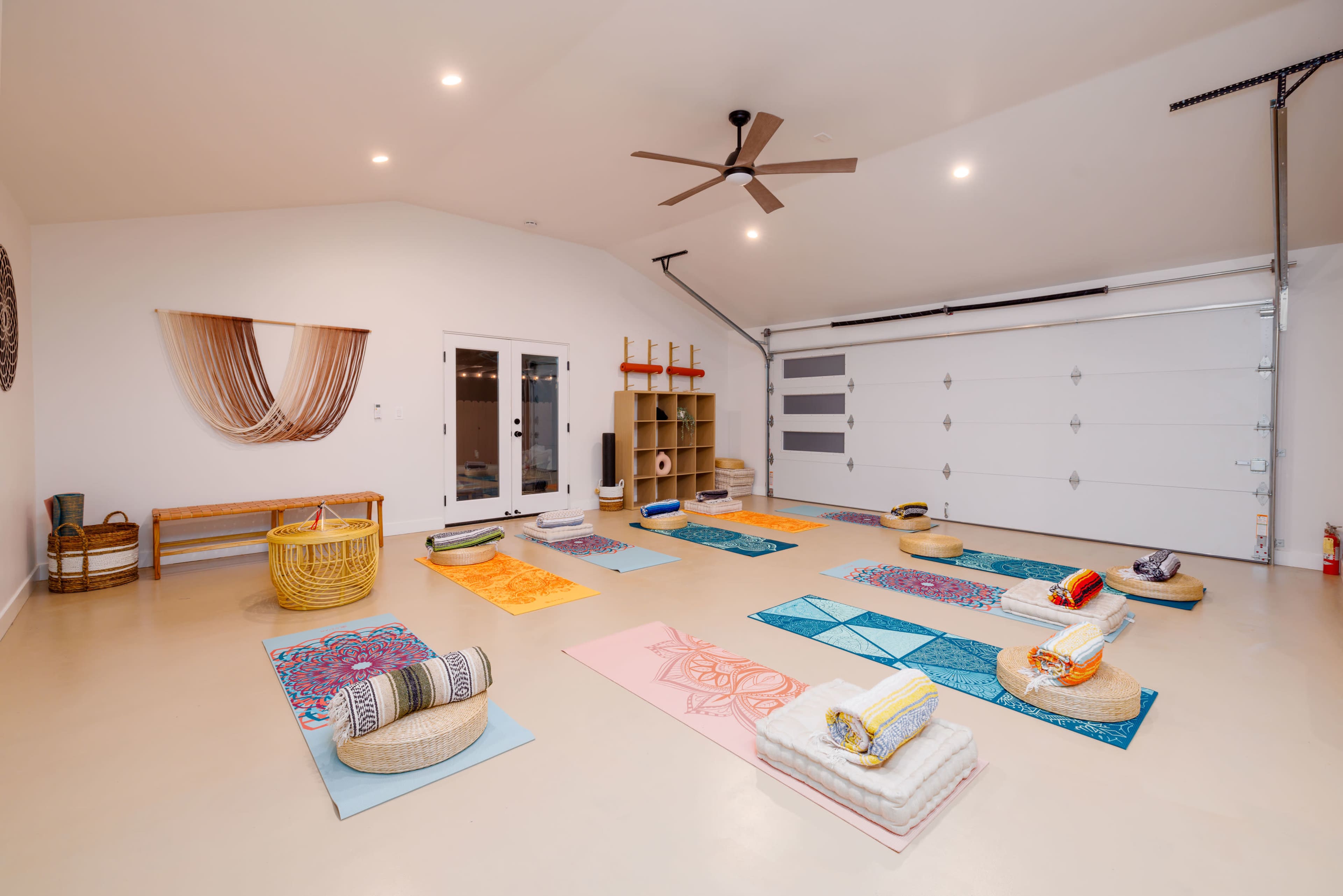A spacious, well-lit yoga studio in a garage with several yoga mats arranged on the floor and props neatly placed nearby.