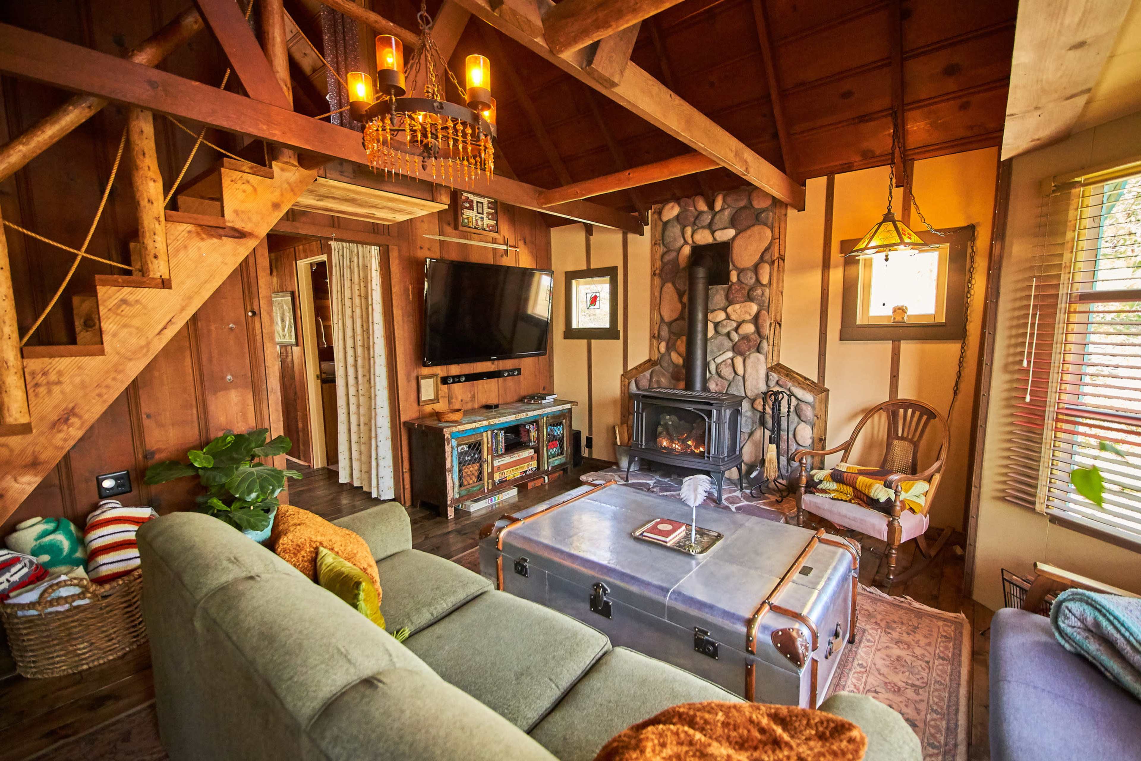 A cozy cabin living room with wooden beams, a stone fireplace, and a mix of vintage and modern furnishings.